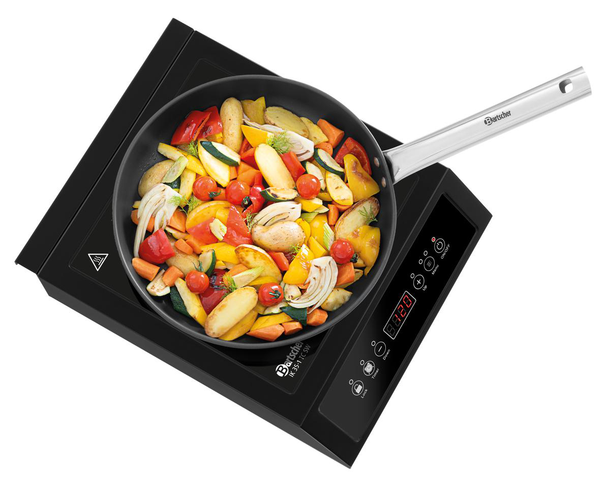 Ein Kochfeld mit einer Pfanne voller bunter Gemüsestücke, darunter Kartoffeln, Zucchini und Paprika.