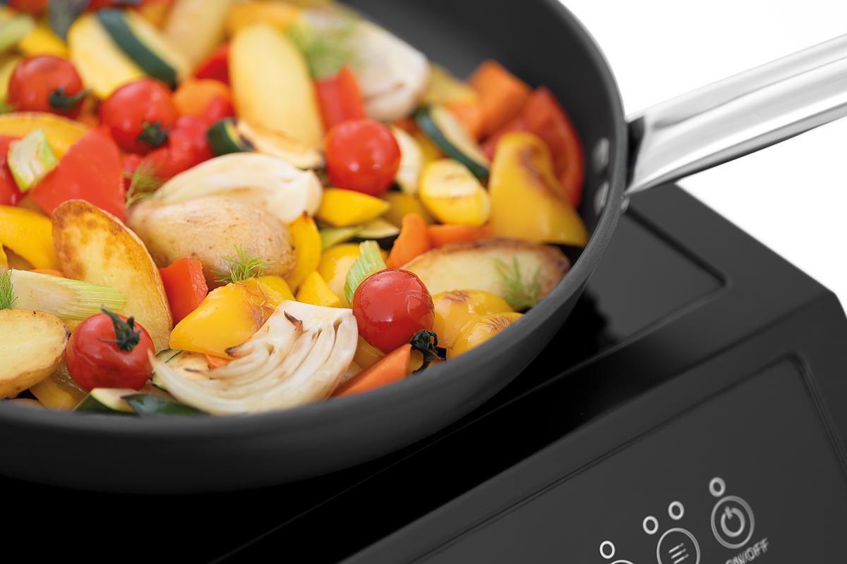 Gemüsepfanne mit Kartoffeln, Paprika, Tomaten und Zucchini auf einem Induktionskochfeld.