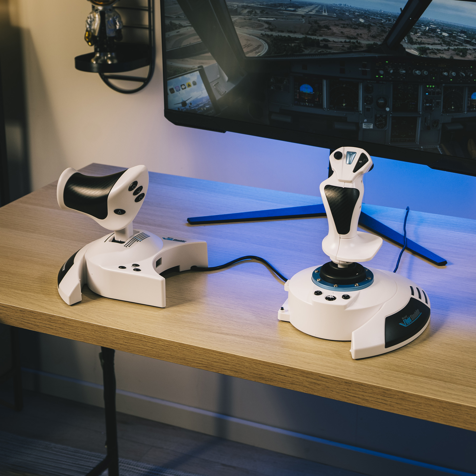 Deux joysticks blancs de simulateur de vol sur un bureau en bois, avec un moniteur affichant une simulation de vol.