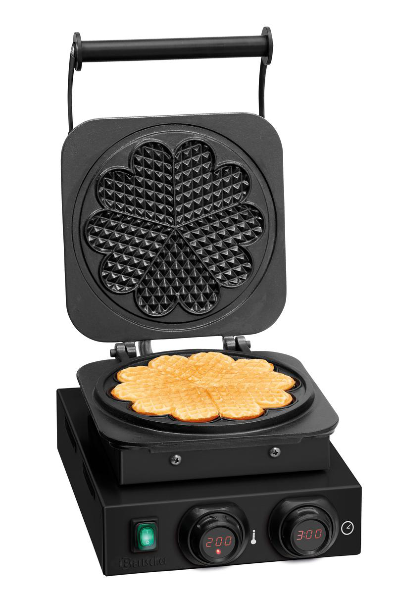 Ein offener Waffelautomat mit einem fertigen Waffelherz und einem Muster oben.