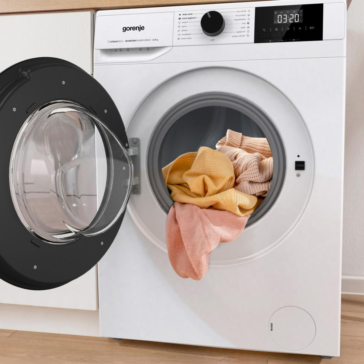 Fehér Gorenje mosógép nyitott ajtóval, benne színes ruhákkal.