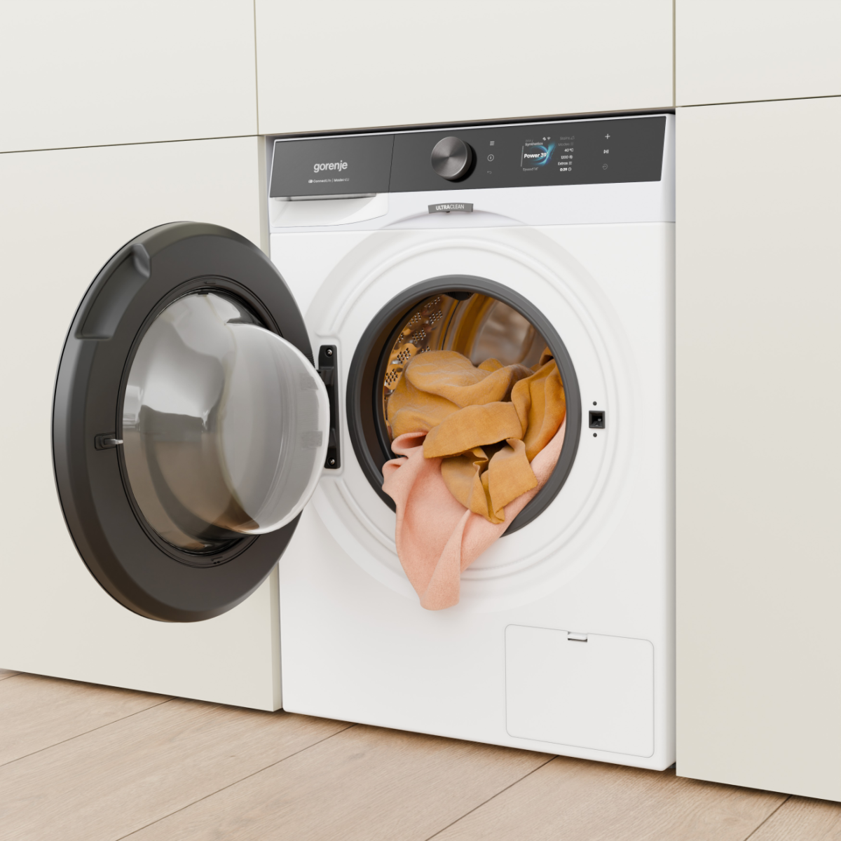 Fehér Gorenje mosógép nyitott ajtóval, narancssárga és barack színű textíliákkal.