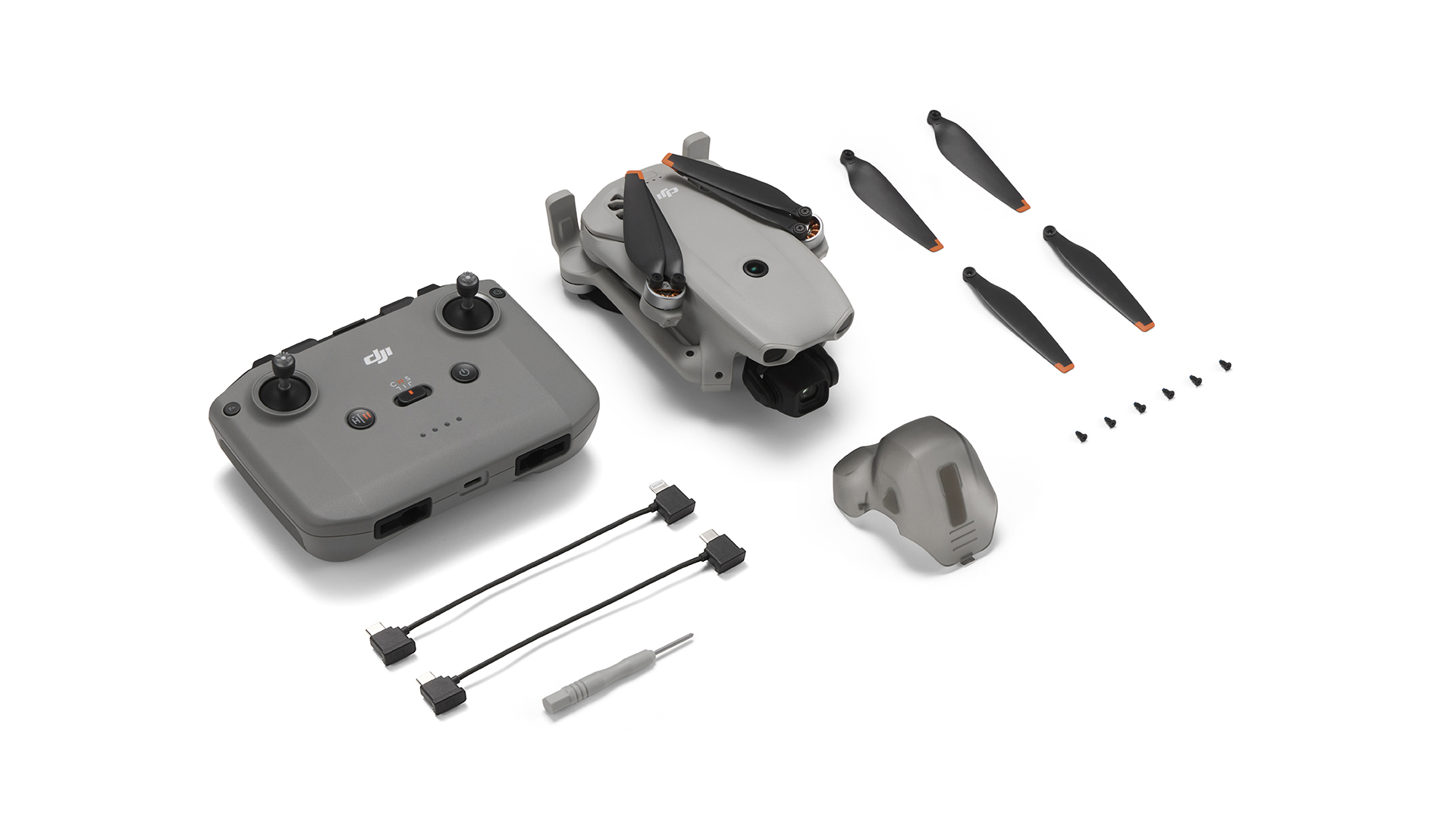 Drone uzaktan kumanda, yedek pervaneler ve aksesuarlarla beyaz arka planda.