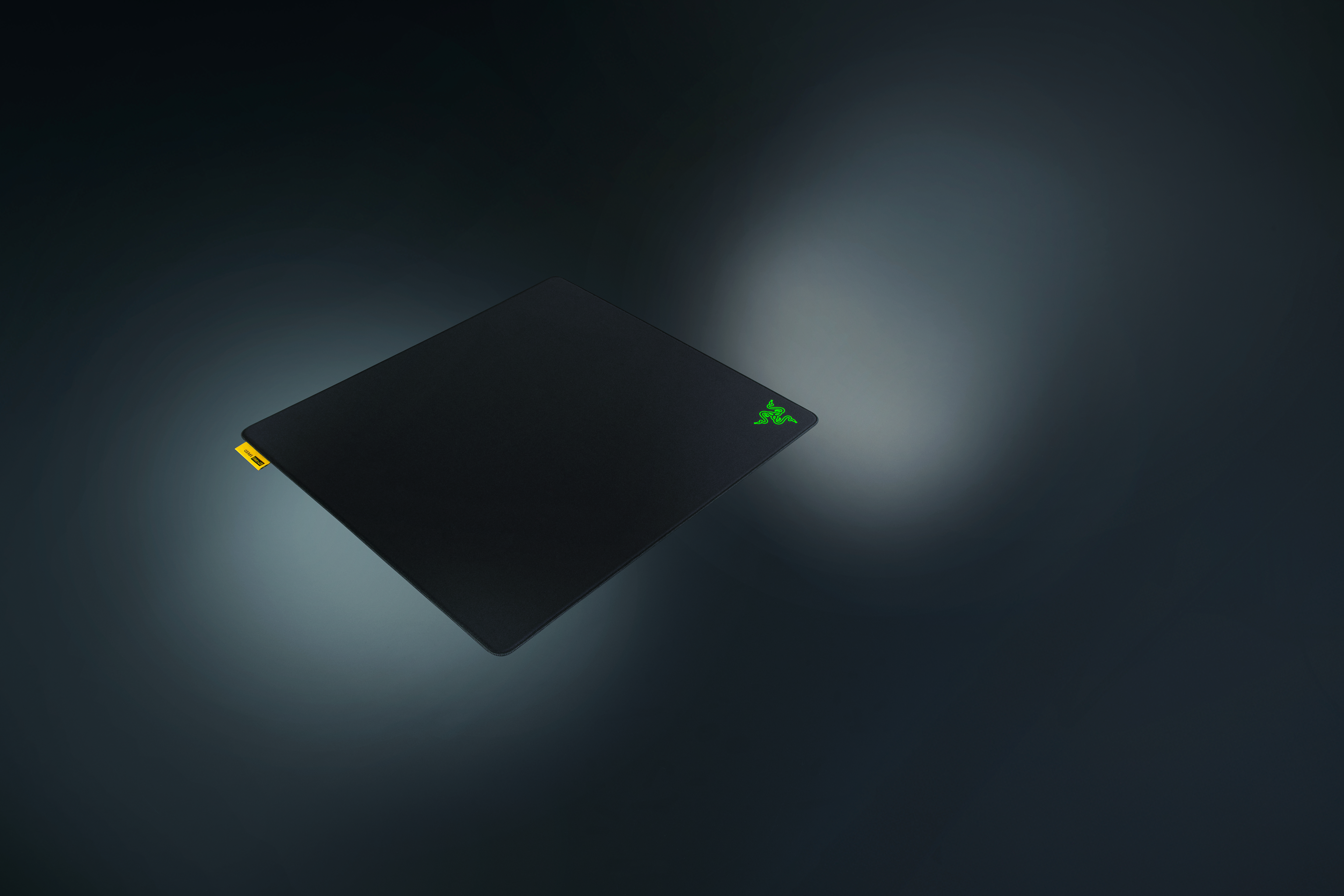 Eine schwarze Razer-Mausmatte mit grünem Logo und gelbem Etikett auf dunklem Hintergrund.