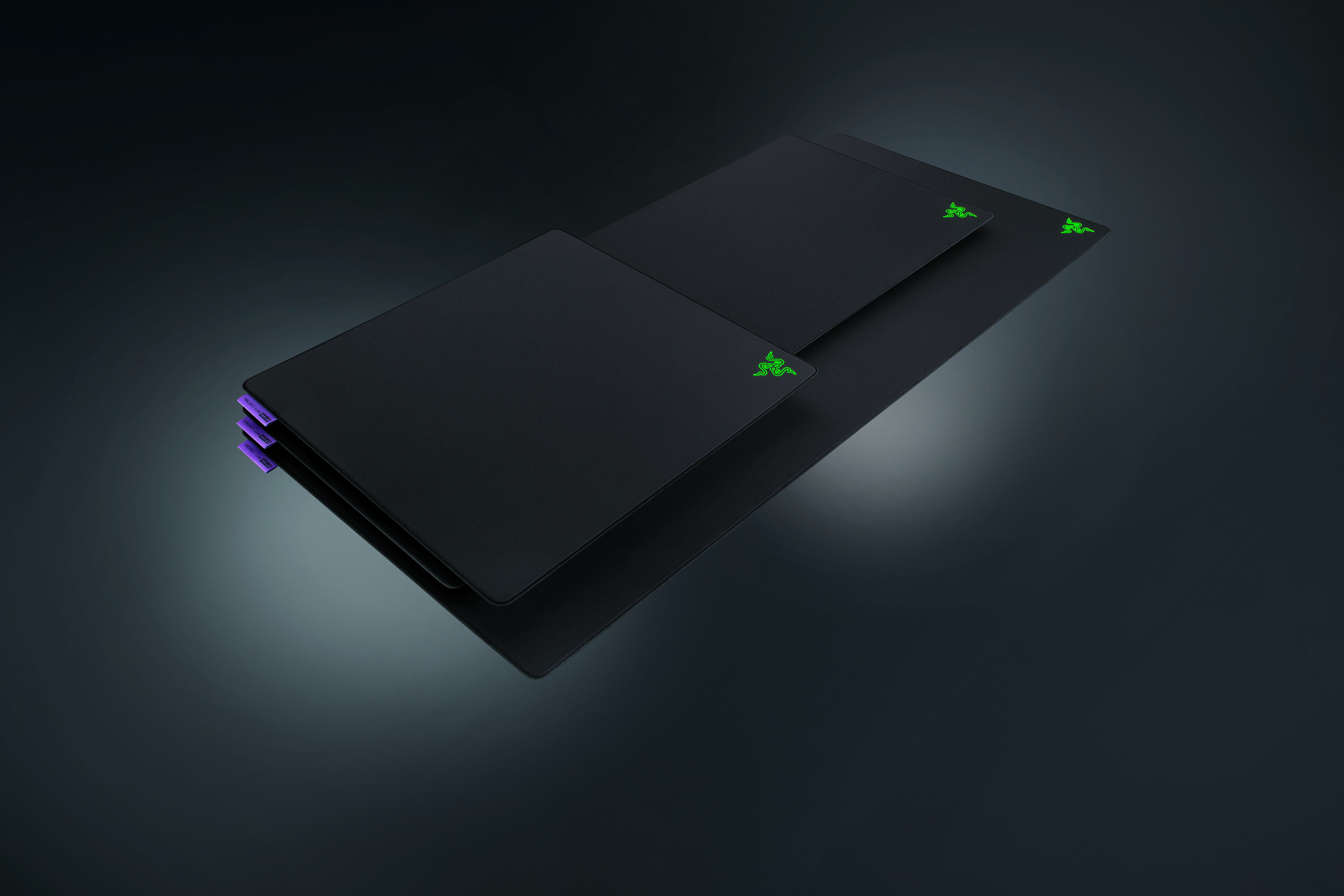 Drei schwarze Razer-Mauspads mit grünen Logos auf dunklem Hintergrund.