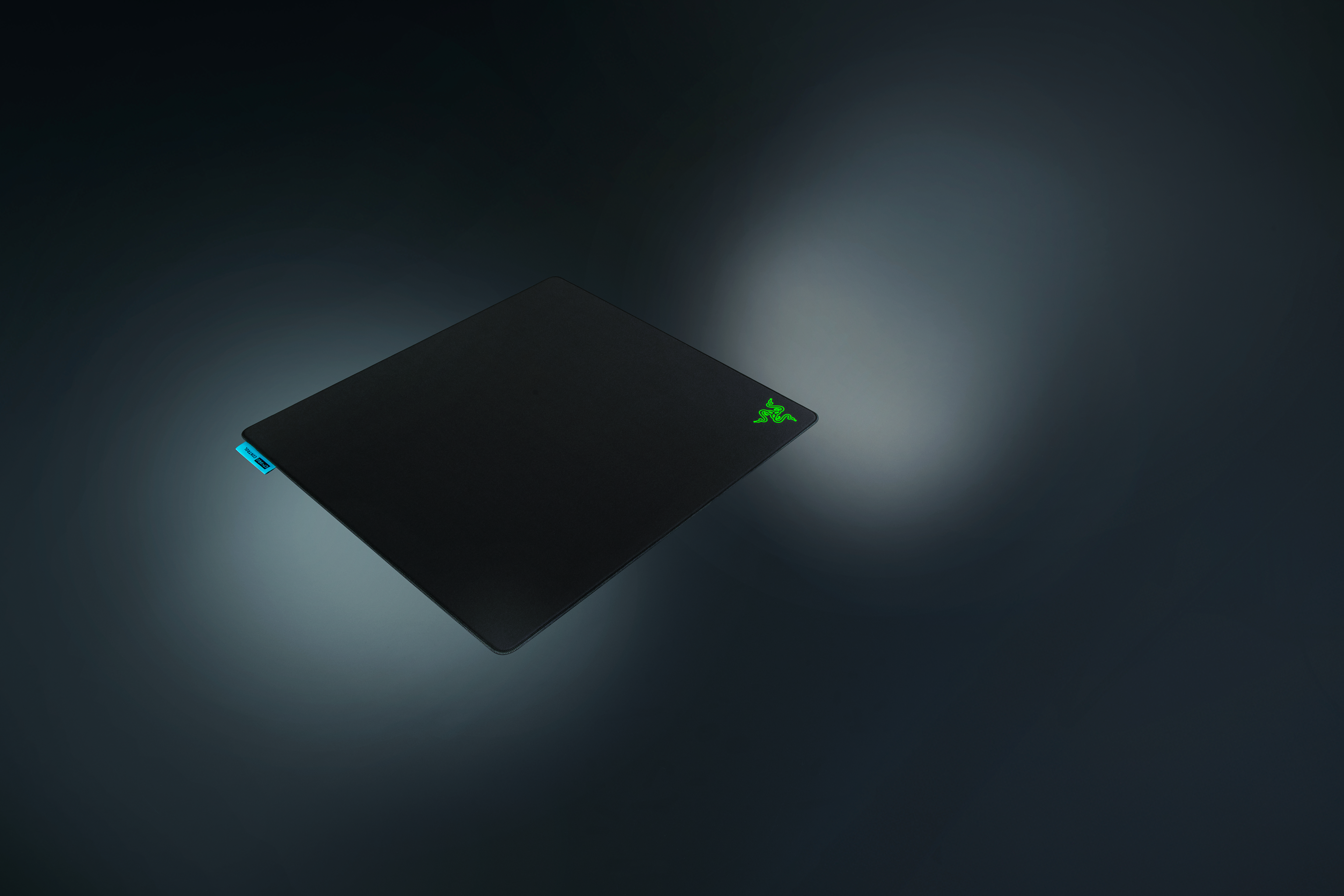 Schwarzes Mauspad mit grünem Logo und blauem Etikett auf dunklem Hintergrund.