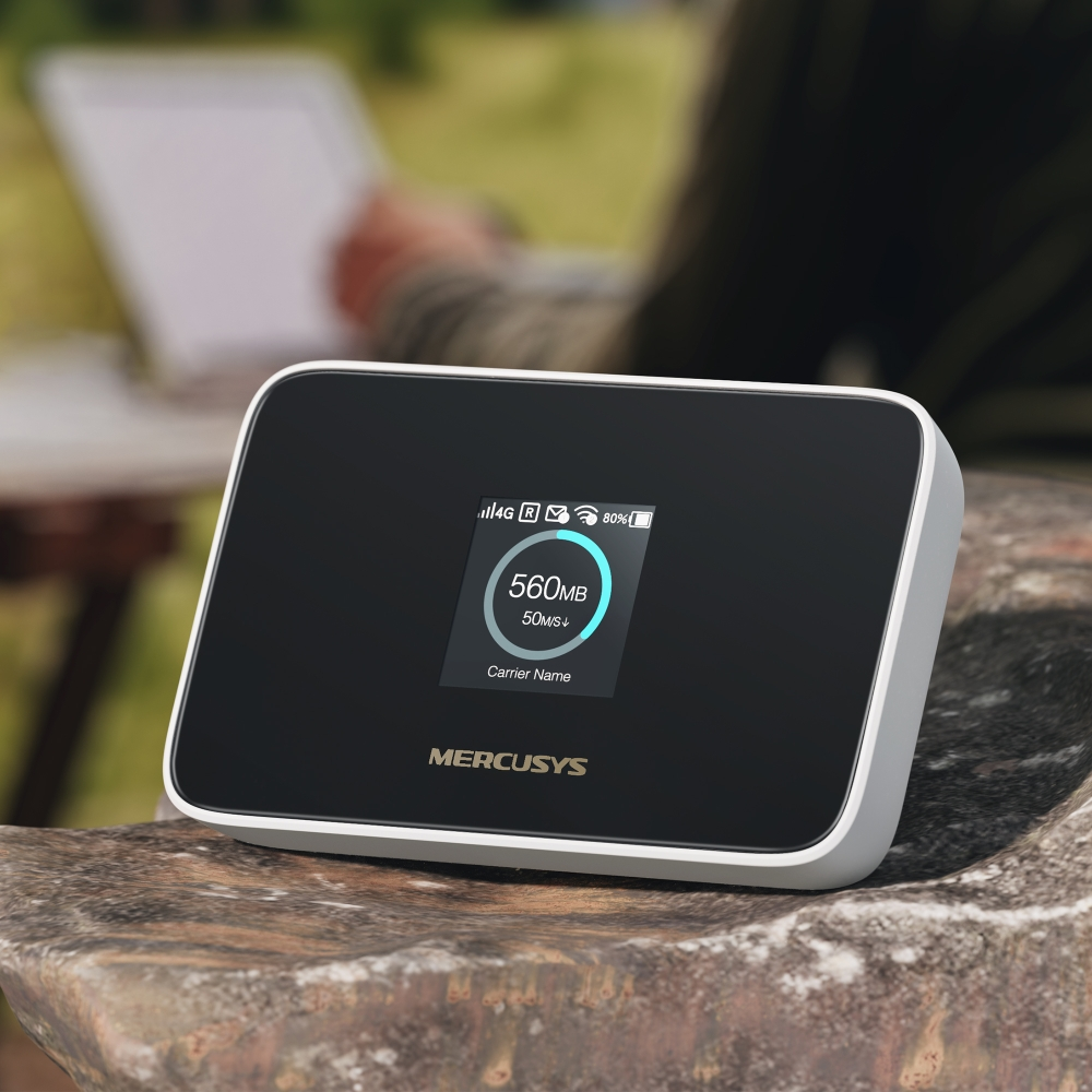 Un hotspot 4G de Mercusys sobre una piedra, persona con portátil al fondo.