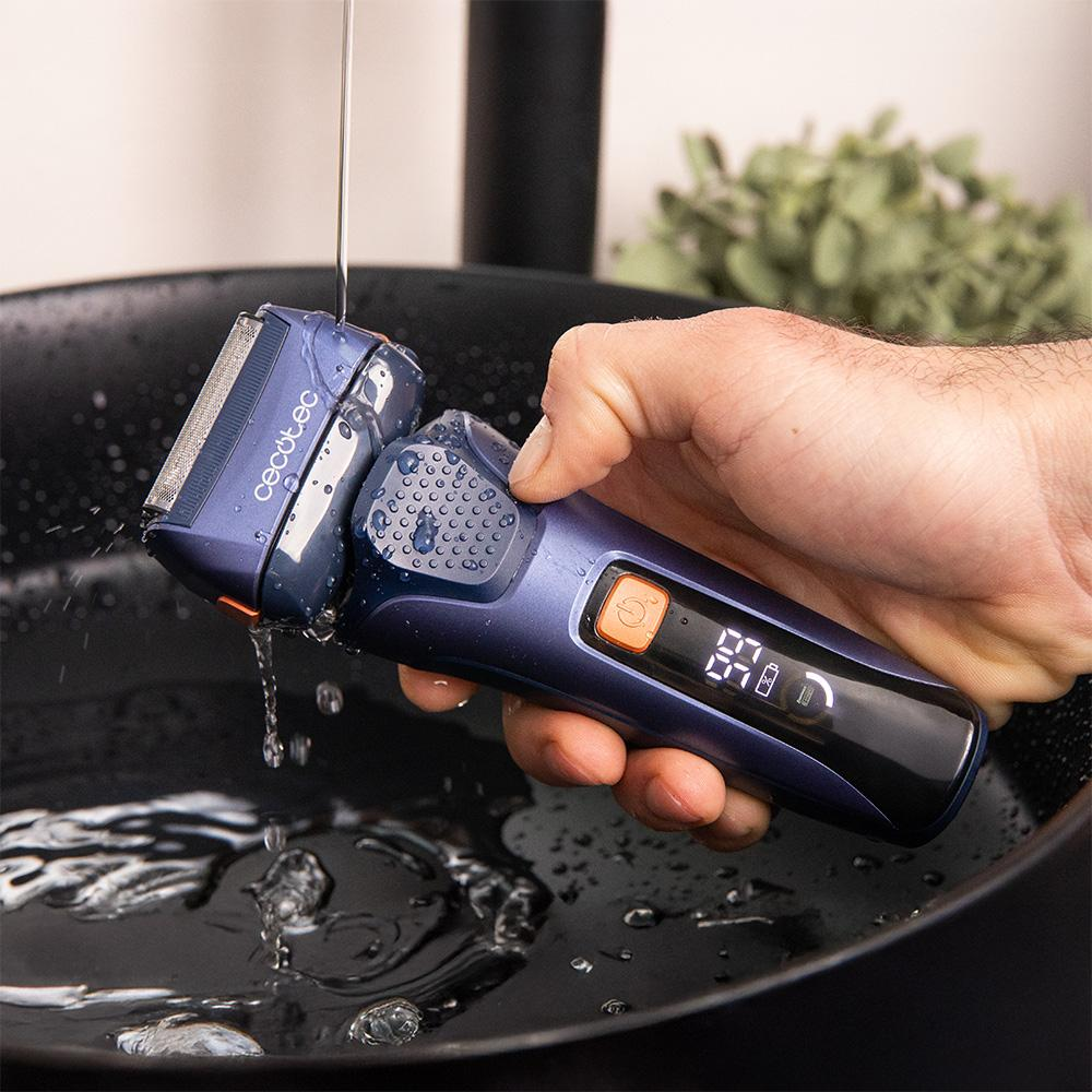 Una afeitadora eléctrica azul se enjuaga bajo agua corriente en un lavabo oscuro.
