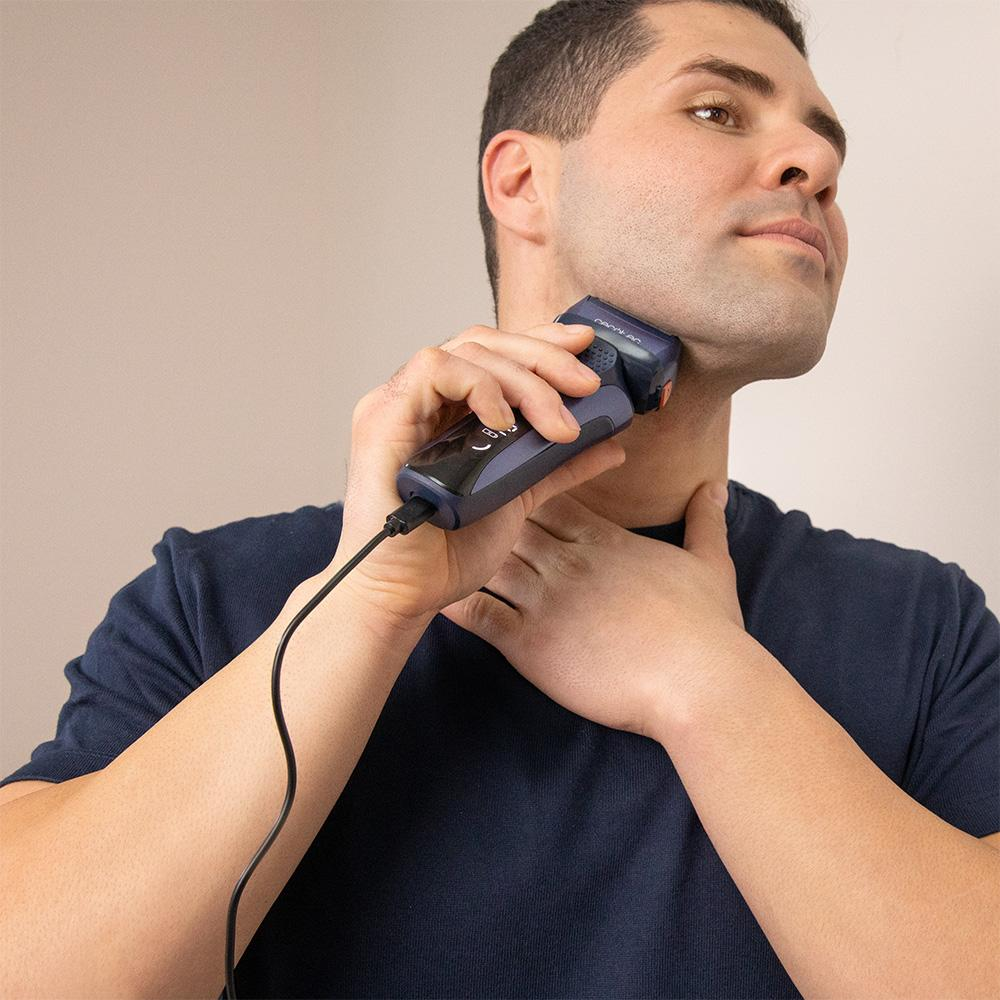 Un hombre se afeita el cuello con una afeitadora eléctrica azul conectada por cable.