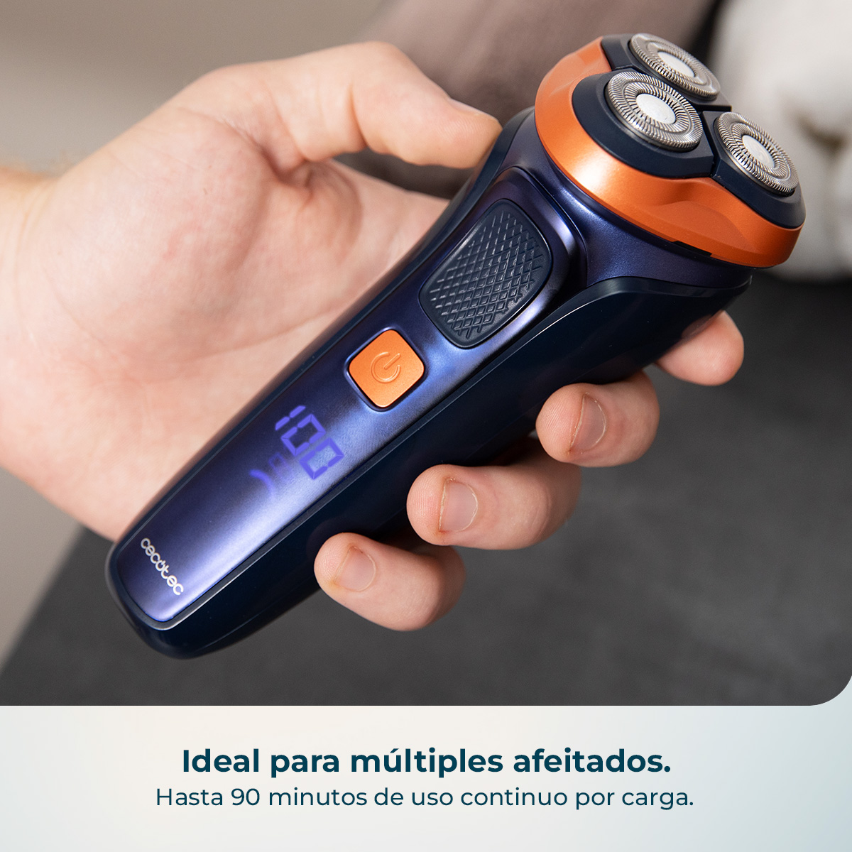 Una mano sostiene una afeitadora eléctrica azul oscuro con detalles naranjas y pantalla digital.