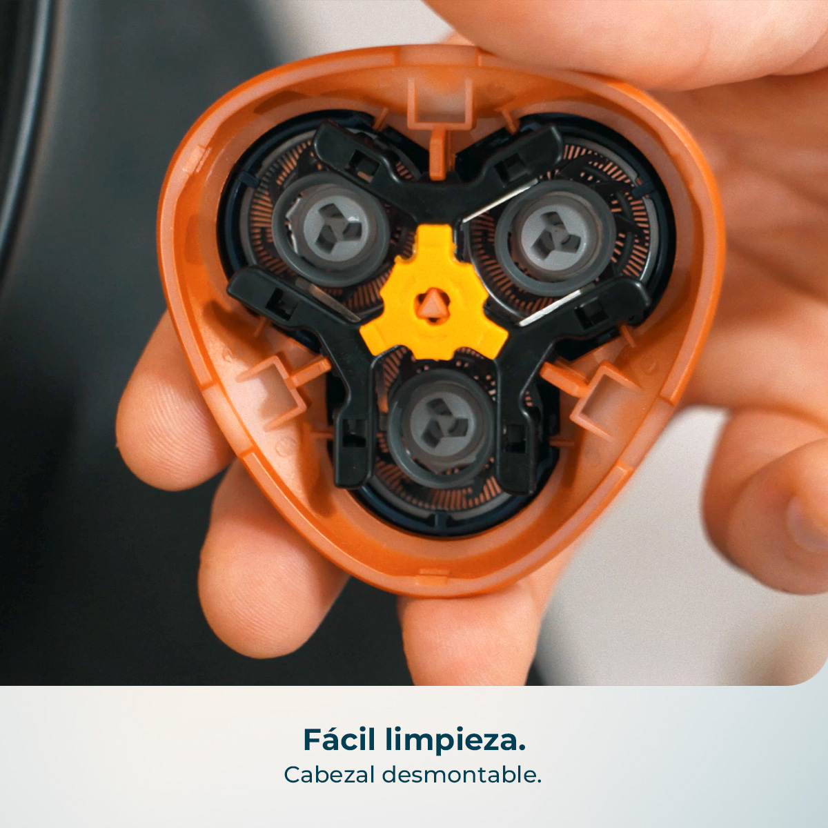 Primer plano de una persona sosteniendo un cabezal de afeitadora eléctrica naranja con partes internas negras y amarillas.