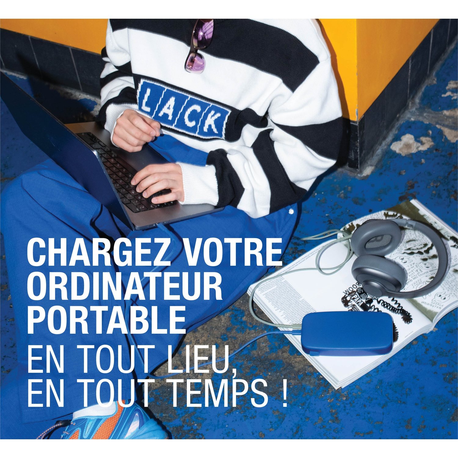 Personne avec ordinateur portable, casque et batterie externe sur sol bleu.