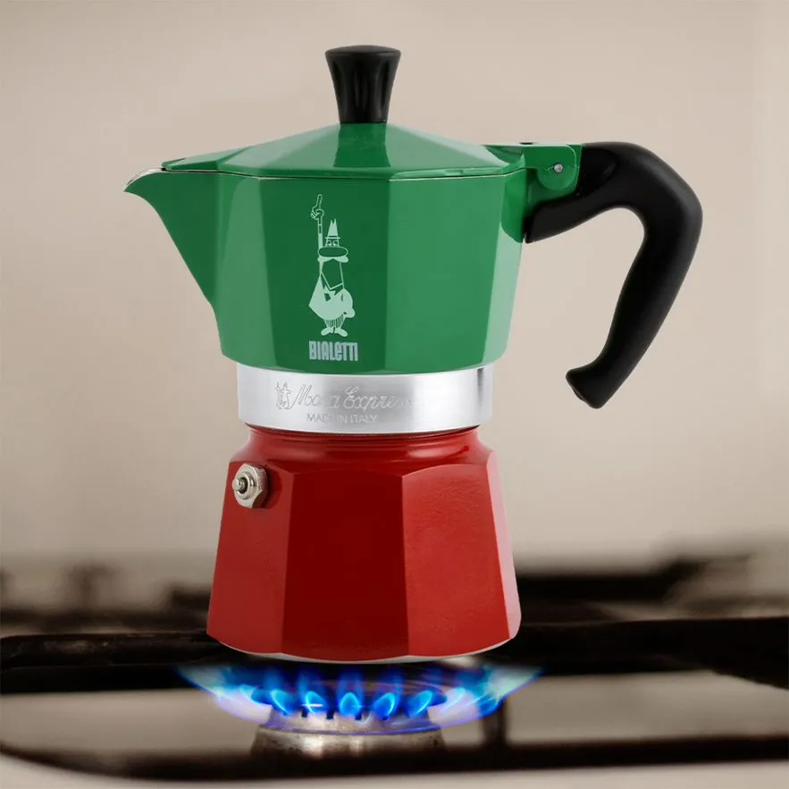 Egy piros és zöld Bialetti kotyogós kávéfőző kék lánggal gáztűzhelyen áll.