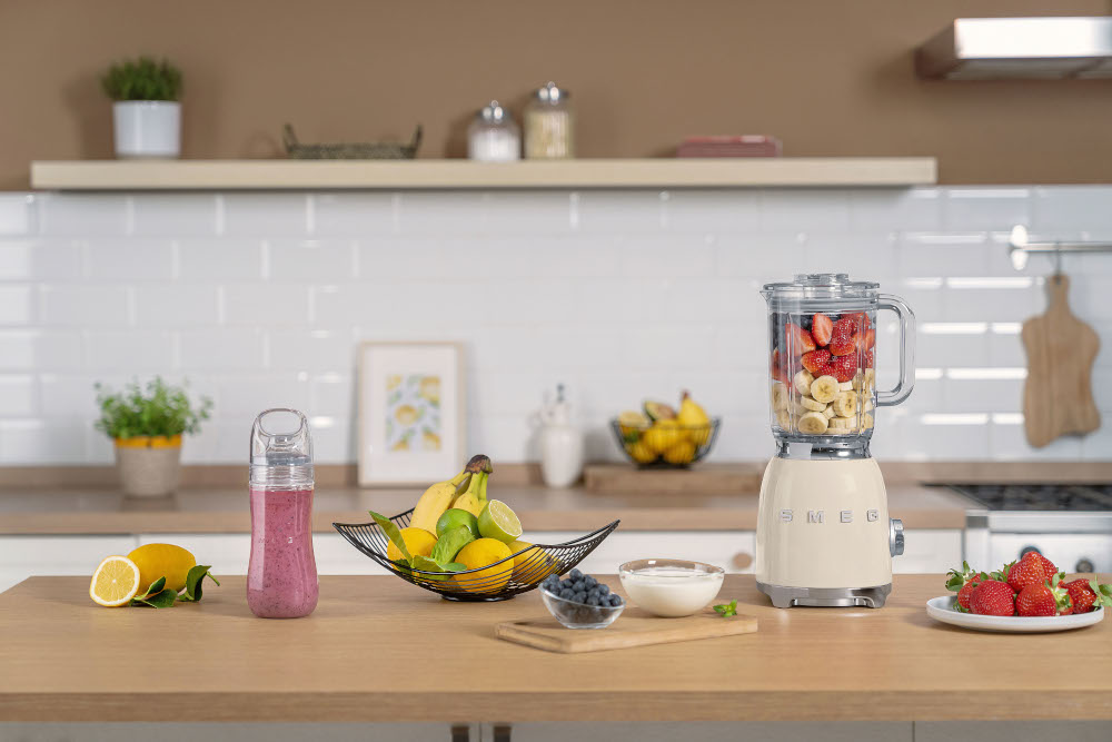 A cream SMEG blender with fruit. A smoothie bottle sits to the left.