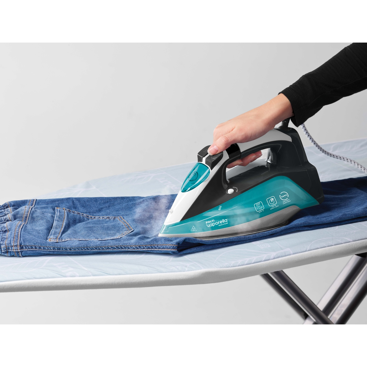 Una mano stira un jeans blu con un ferro da stiro turchese su un asse da stiro.