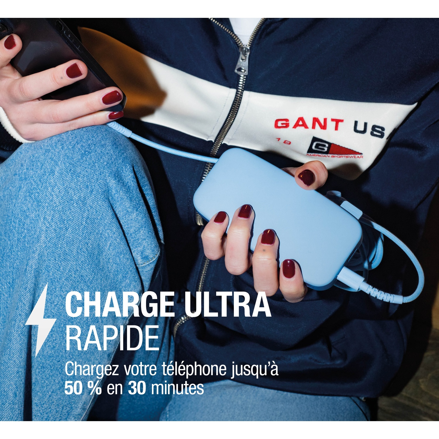 Une personne charge un téléphone avec une power bank bleue et un câble. Logo Gant.