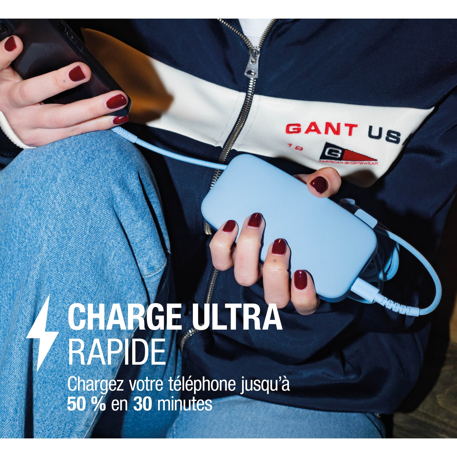 Personne chargeant un téléphone avec une power bank. Jean bleu, veste Gant sombre.