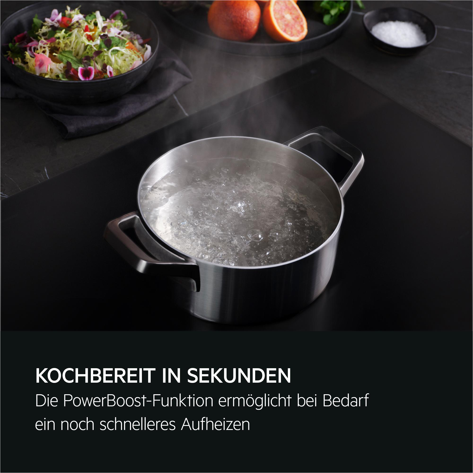 Ein silberner Topf mit kochendem Wasser auf einem schwarzen Kochfeld.