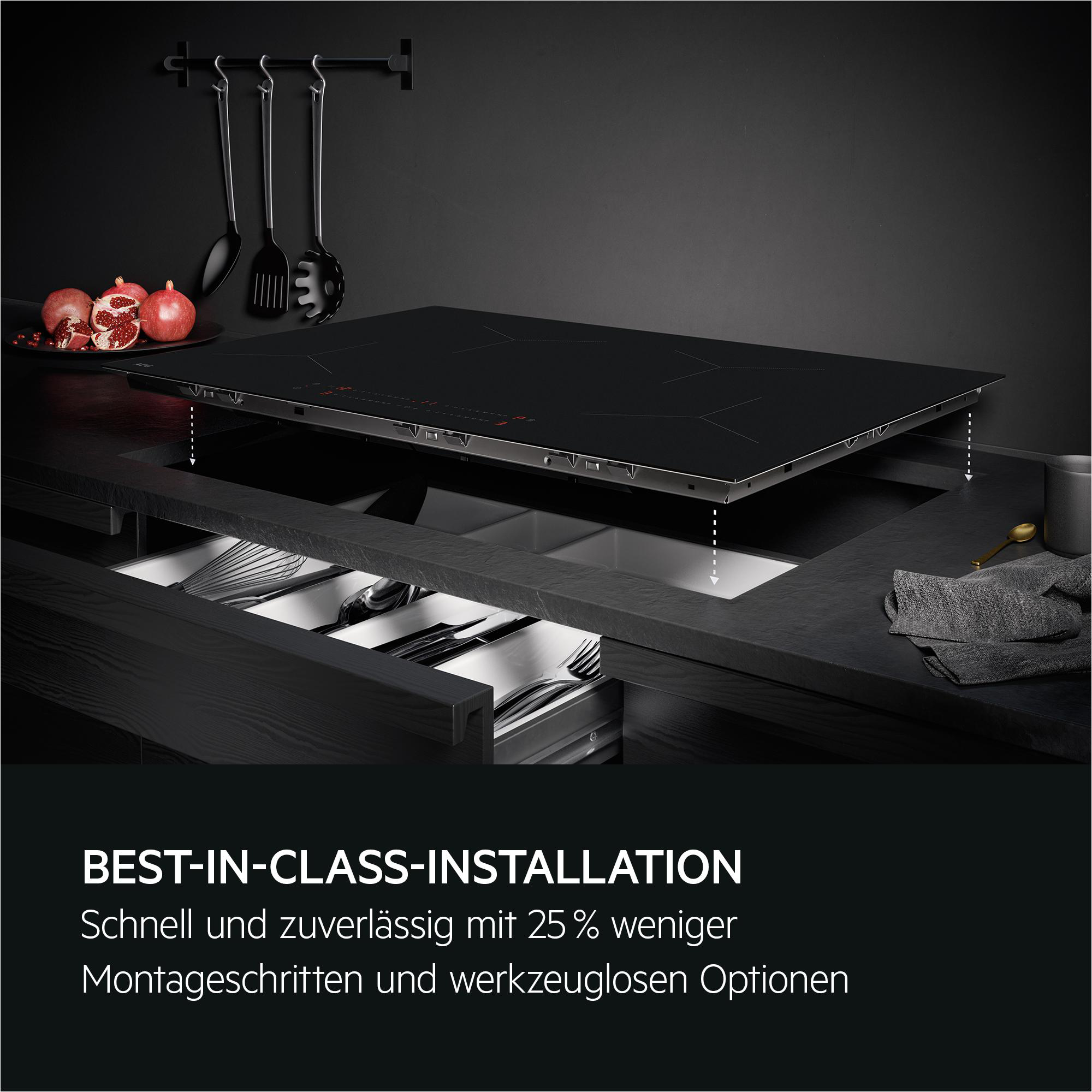 Schwarze Induktionskochplatte über Schublade mit Besteck. Granatäpfel und Utensilien daneben.