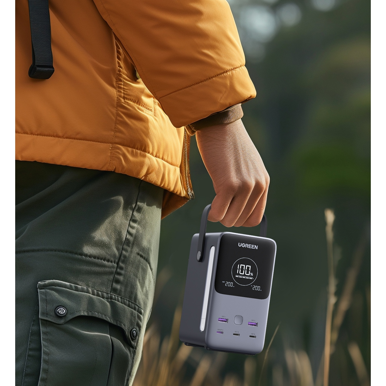 Una mano tiene un power bank UGREEN grigio con carica al 100% all'aperto.