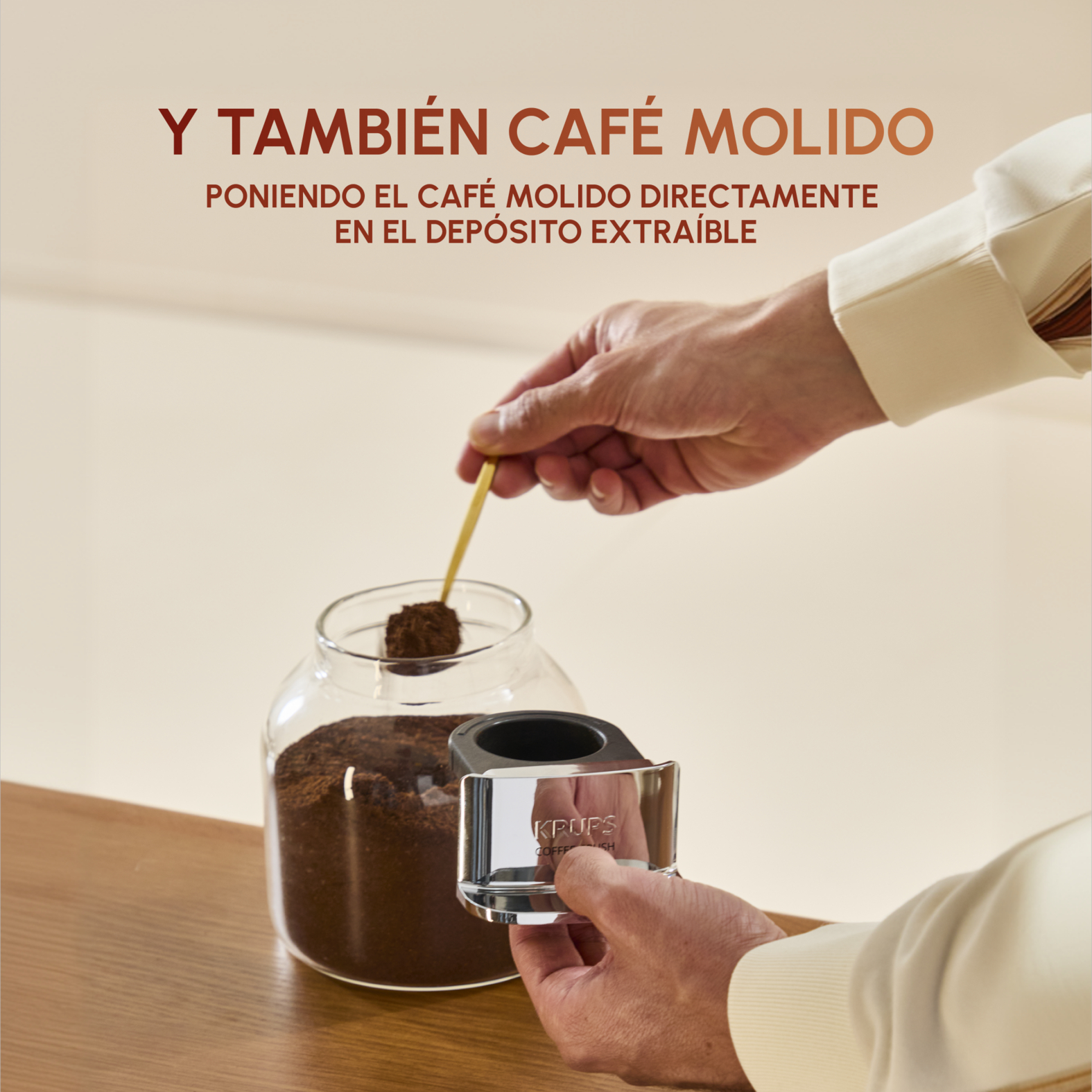 Una mano usa una cuchara para sacar café molido de un tarro de cristal.