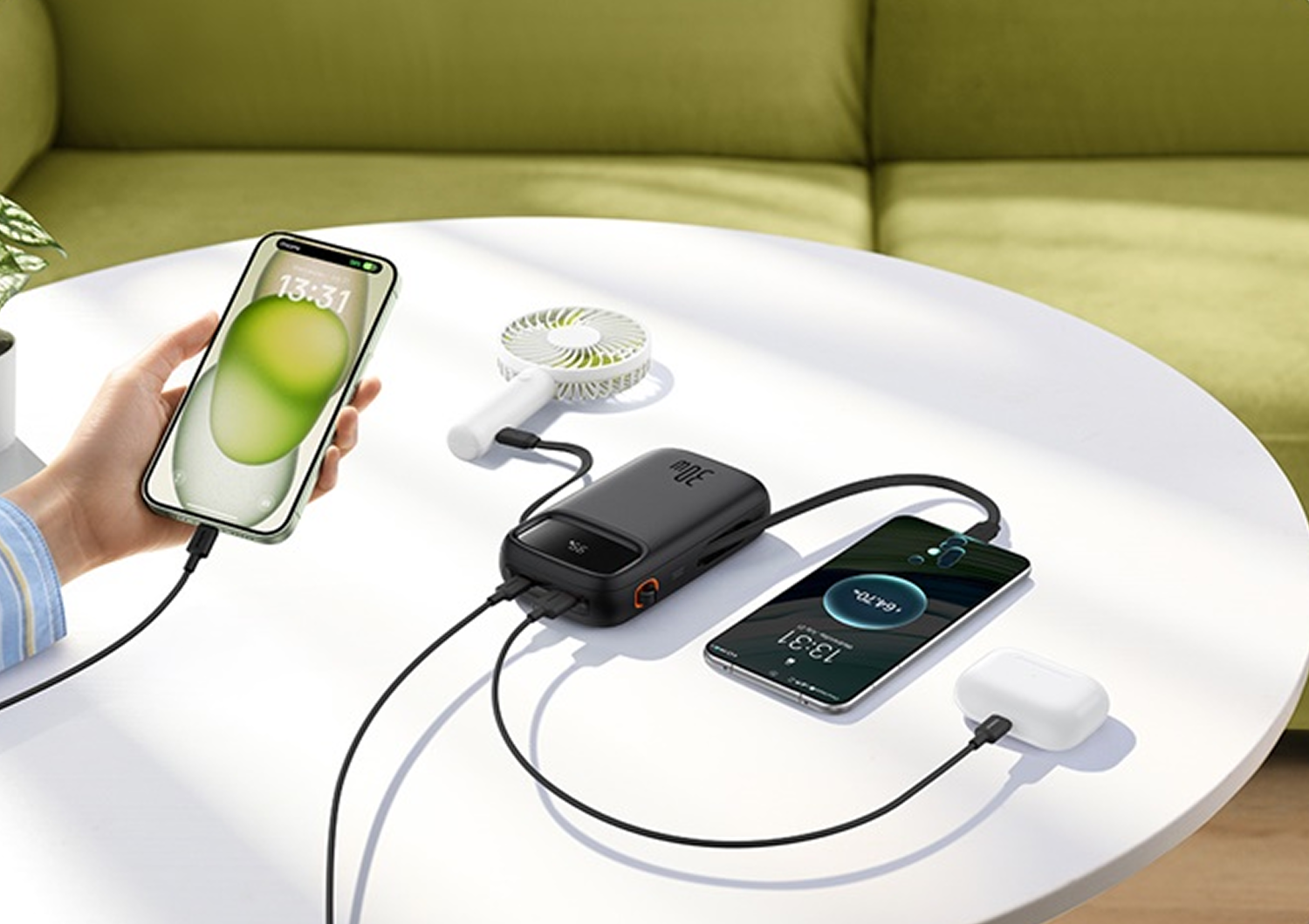 Una power bank negra carga dos teléfonos y un ventilador sobre una mesa blanca.