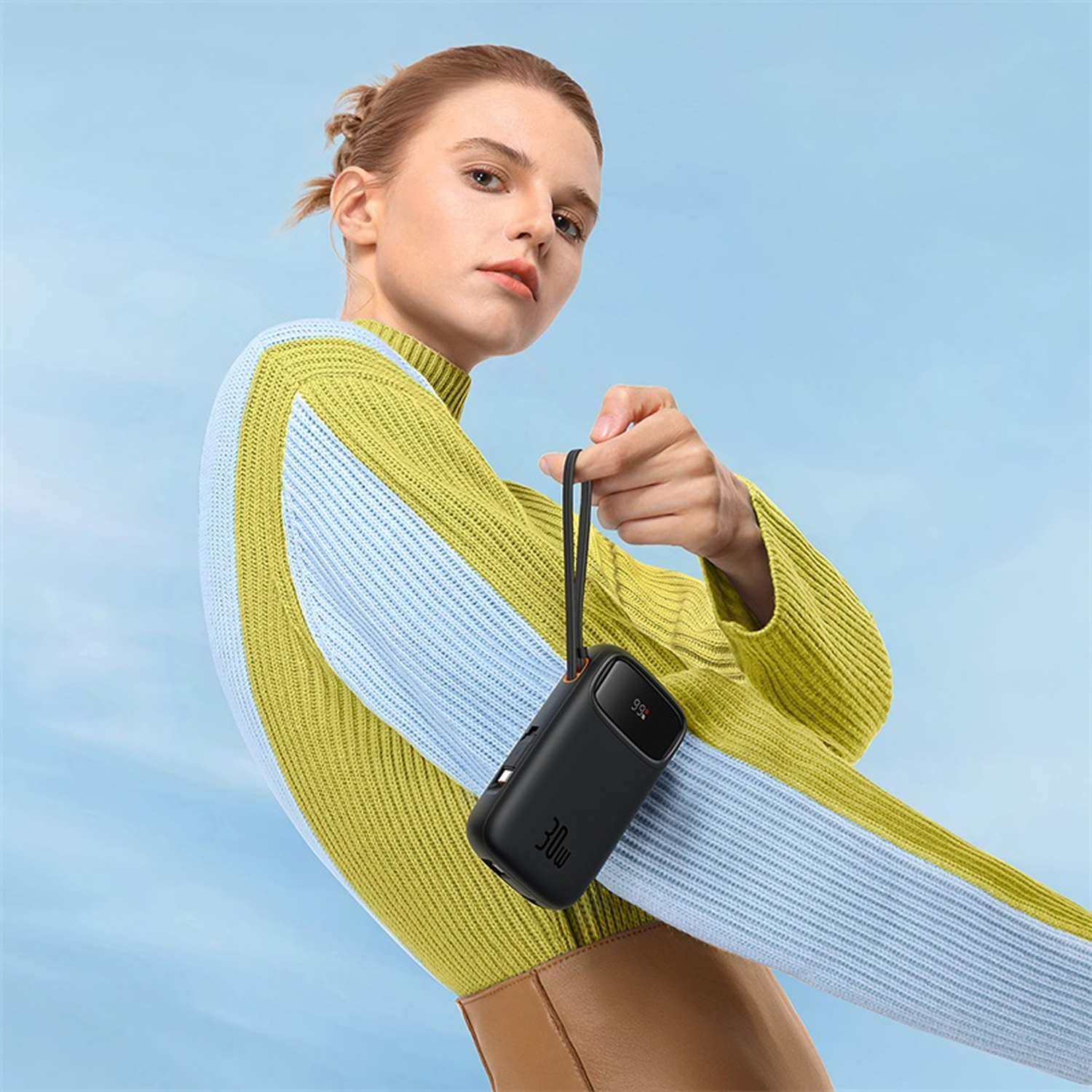 Mujer con suéter a rayas amarillo y azul sostiene banco de energía negro con pantalla de 30W.