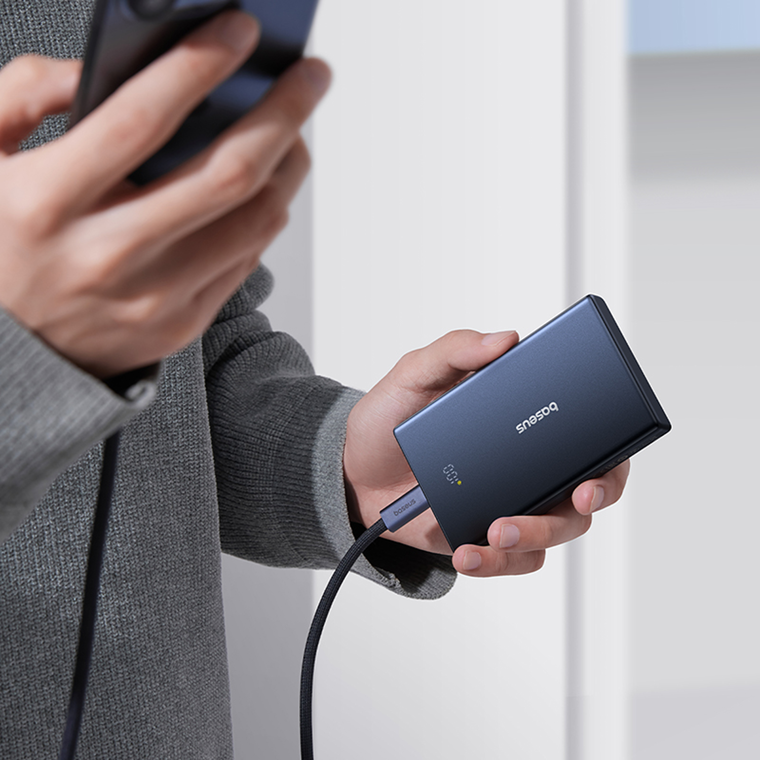 Persona sosteniendo un smartphone y un cargador portátil azul con cable.