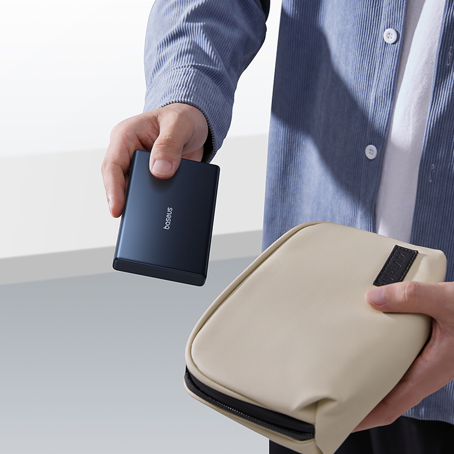 Una persona sostiene un banco de energía oscuro y una bolsa beige.