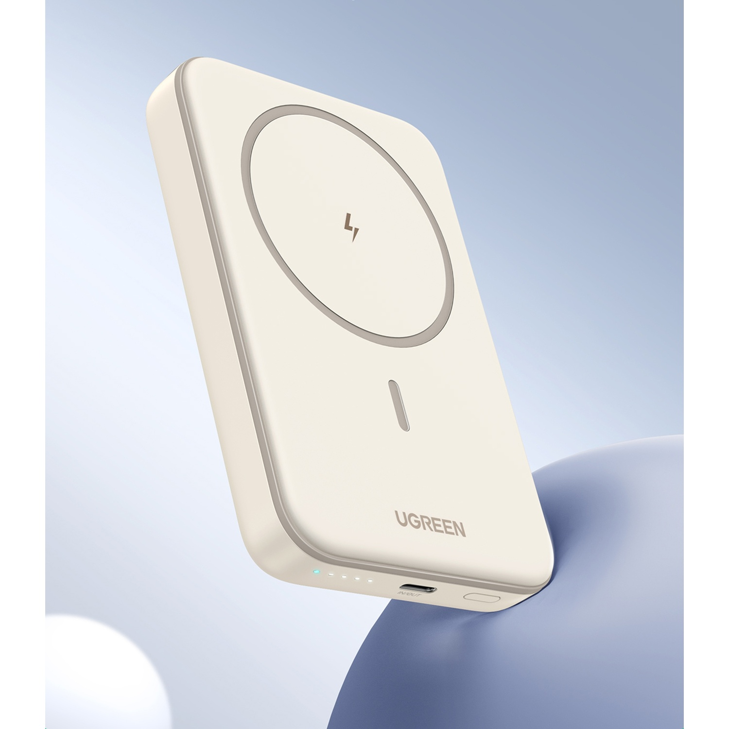 Un power bank UGREEN color crema con indicatori di carica e porta USB-C su superficie blu.