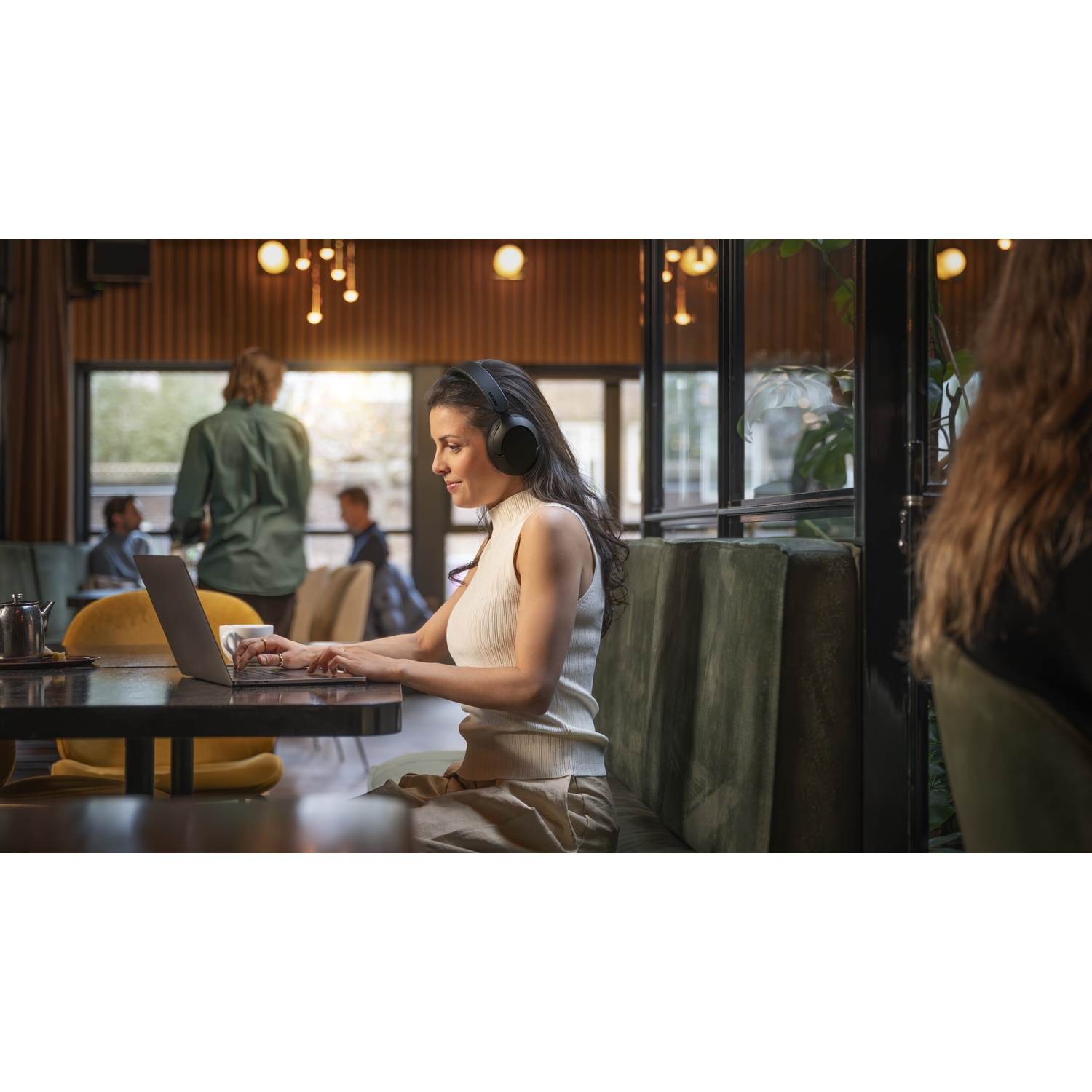 Una donna con cuffie digita su un laptop in un caffè scarsamente illuminato.