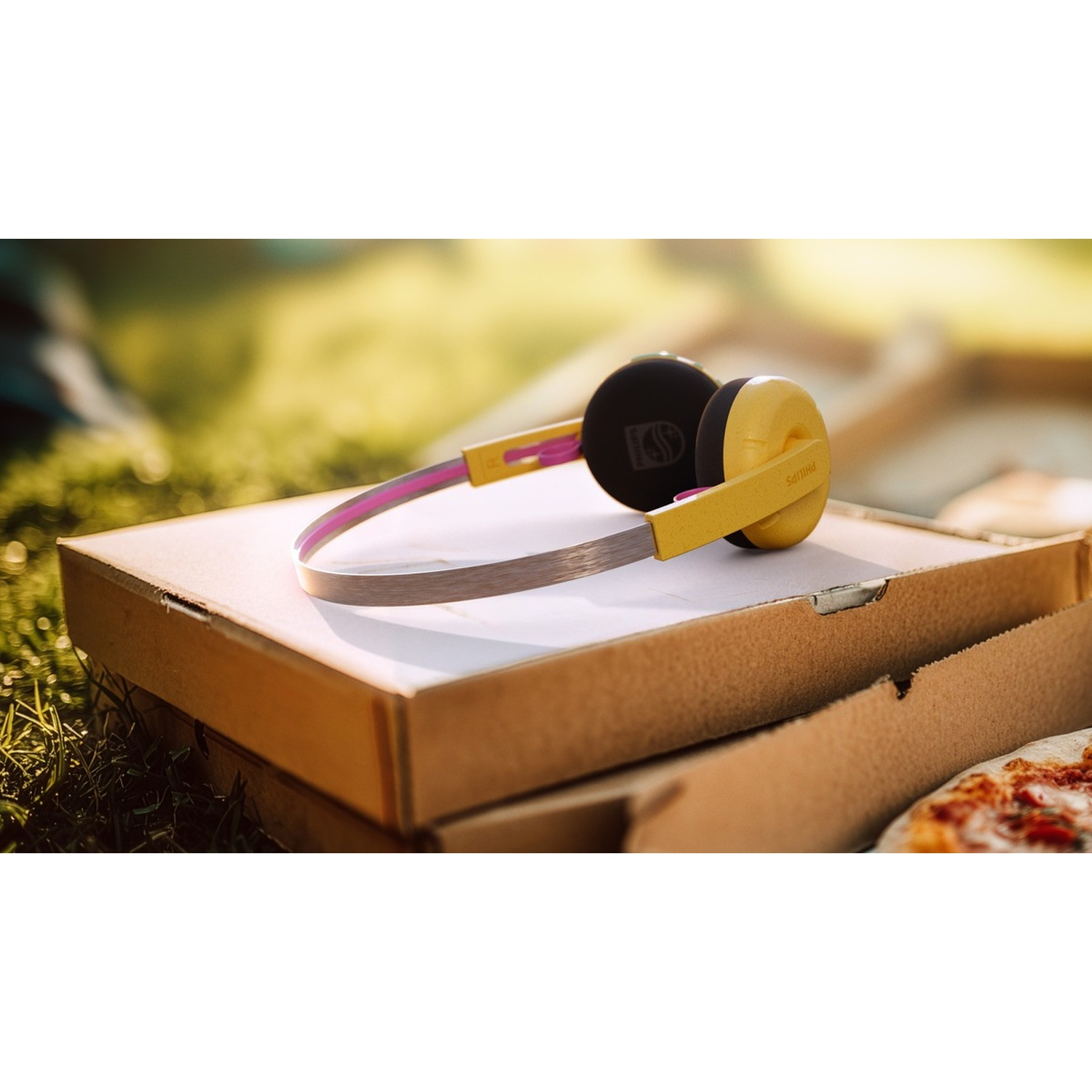 Cuffie Philips gialle su una scatola da pizza all'aperto. Erba e sfondo sfocato.