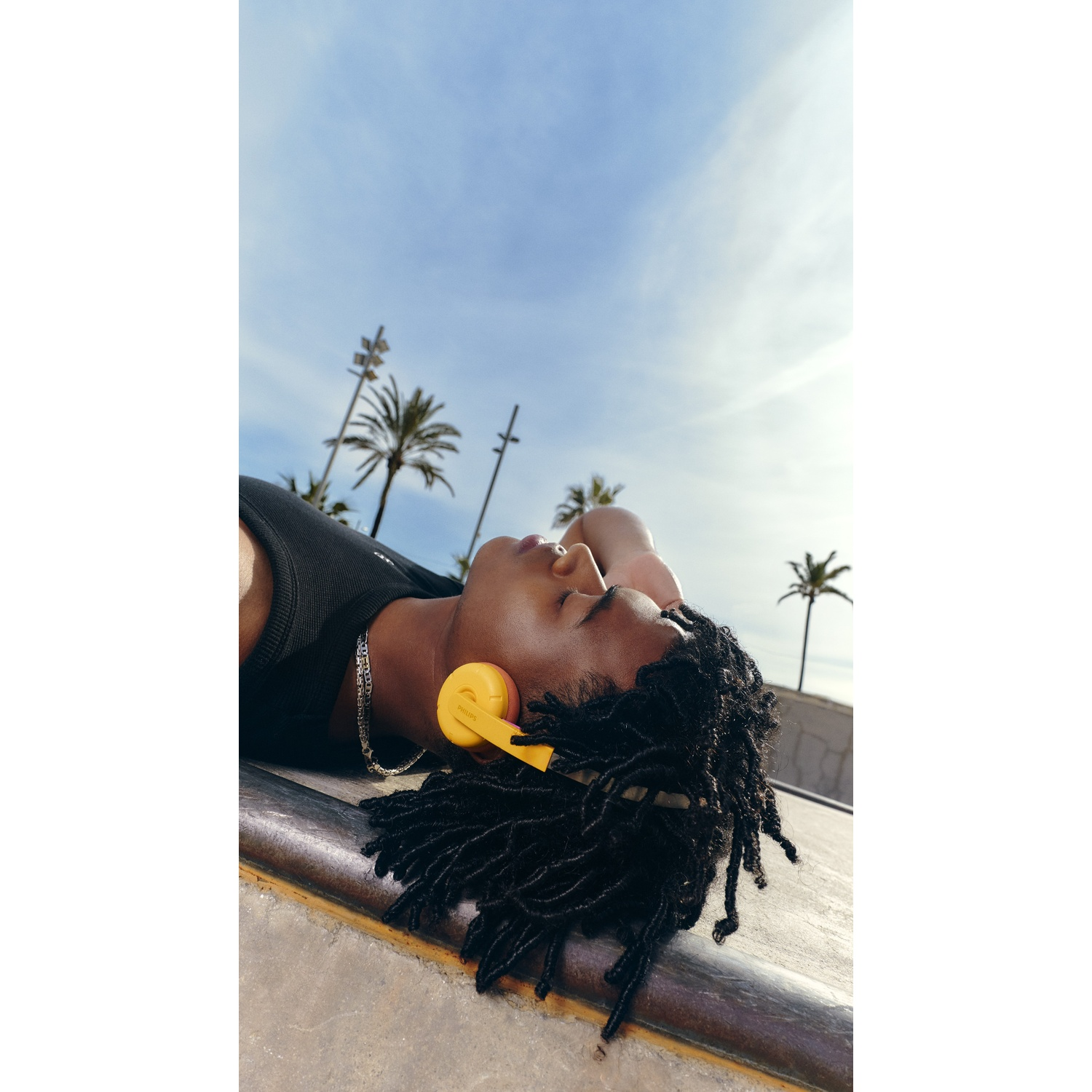 Un uomo con dreadlocks e cuffie gialle giace all'aperto.