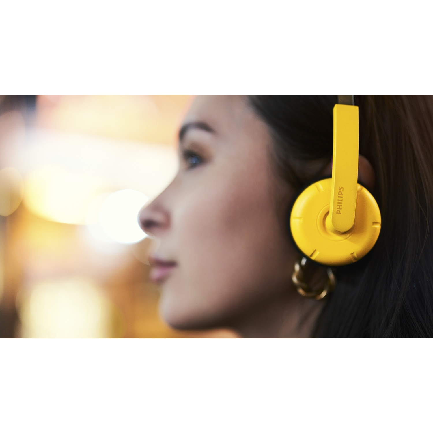Primo piano di una donna con cuffie Philips gialle e orecchini d'oro.