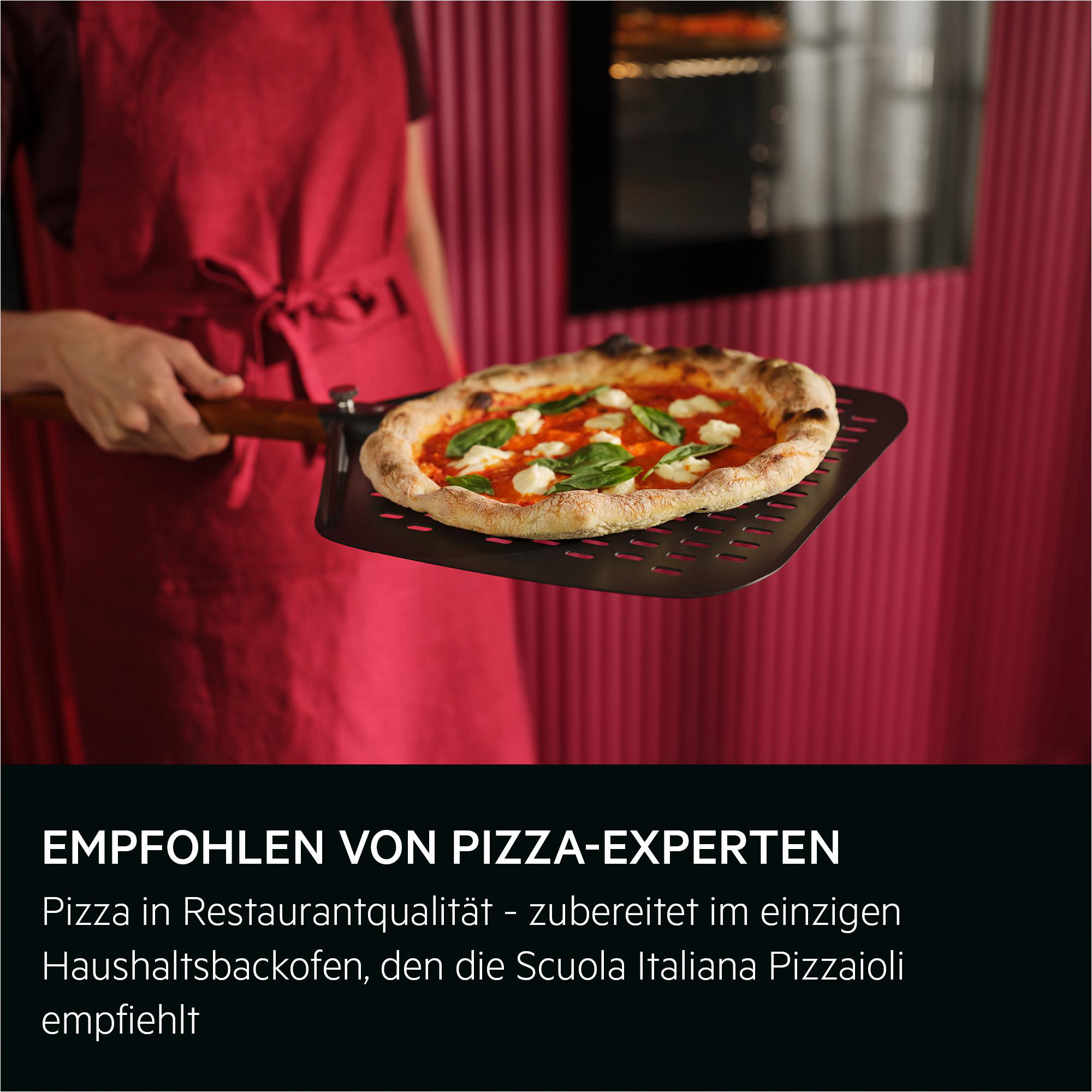 Eine Person in roter Schürze hält eine Pizza auf einem Pizzaschieber.