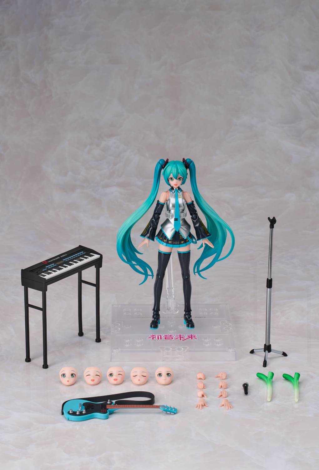 Una figura de Miku Hatsune con accesorios como teclado, guitarra, micrófono y caras.