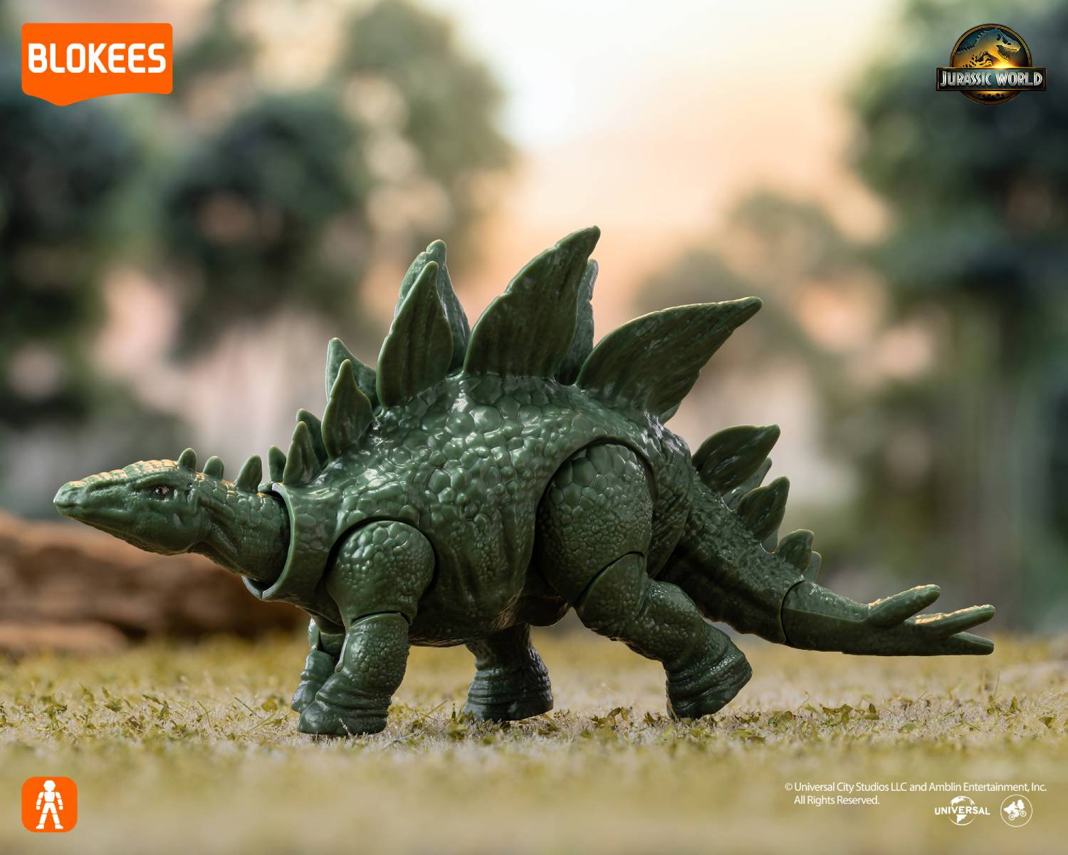 Figura de juguete Stegosaurus verde al aire libre sobre hierba con árboles detrás.