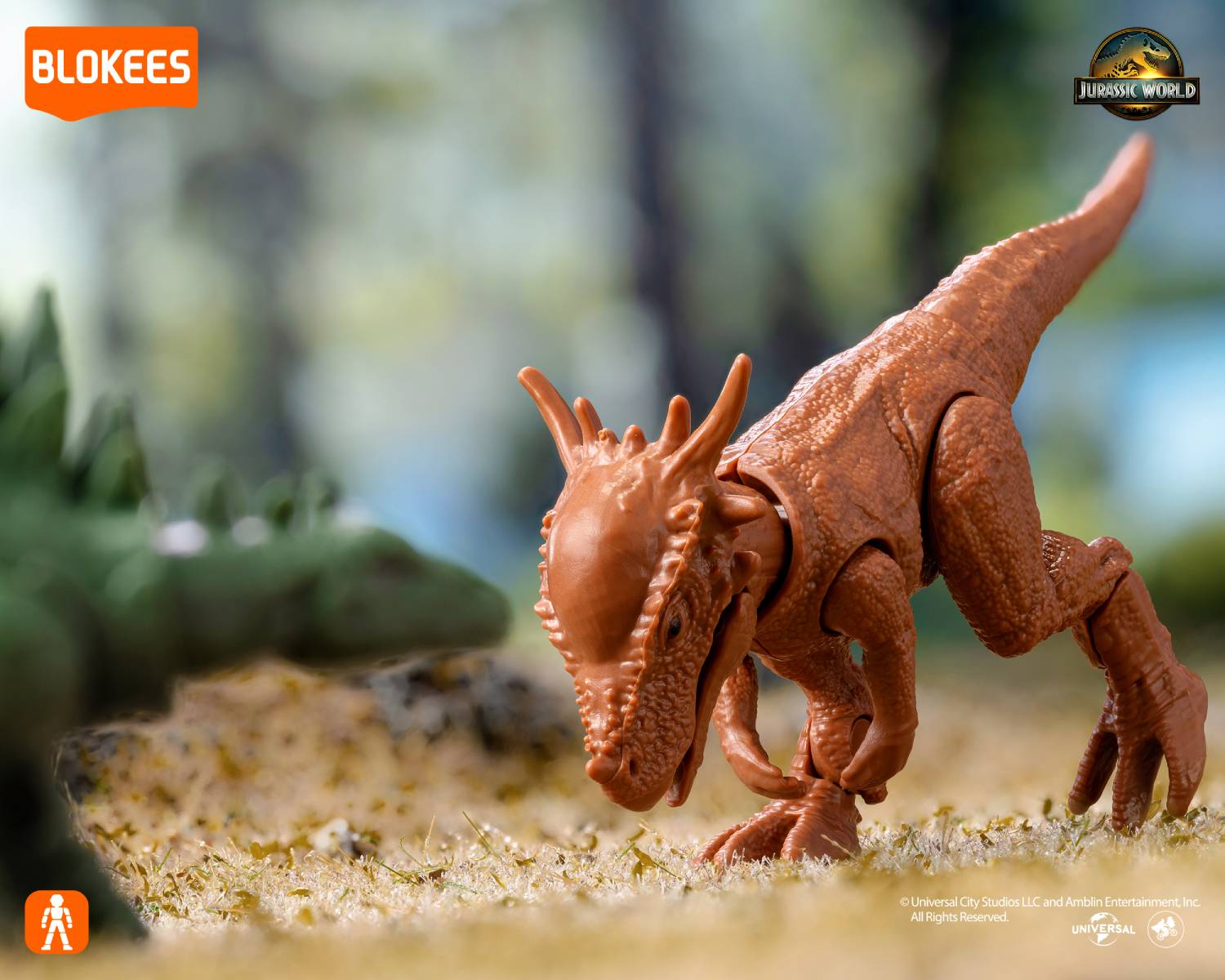 Un juguete de dinosaurio marrón sobre hierba, con un dinosaurio verde al fondo.