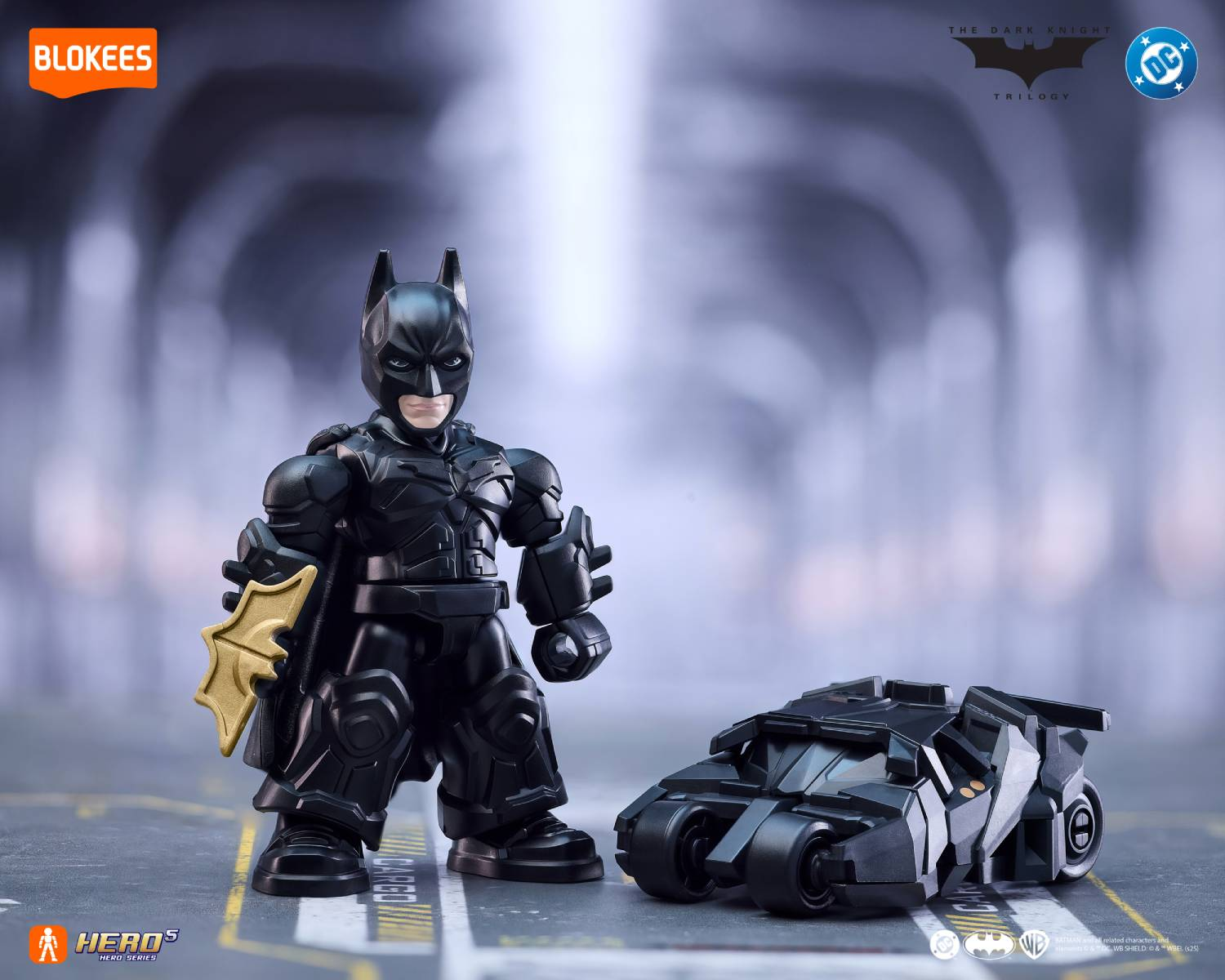Una figura de Batman con un batarang junto a un juguete del Batmóvil negro.