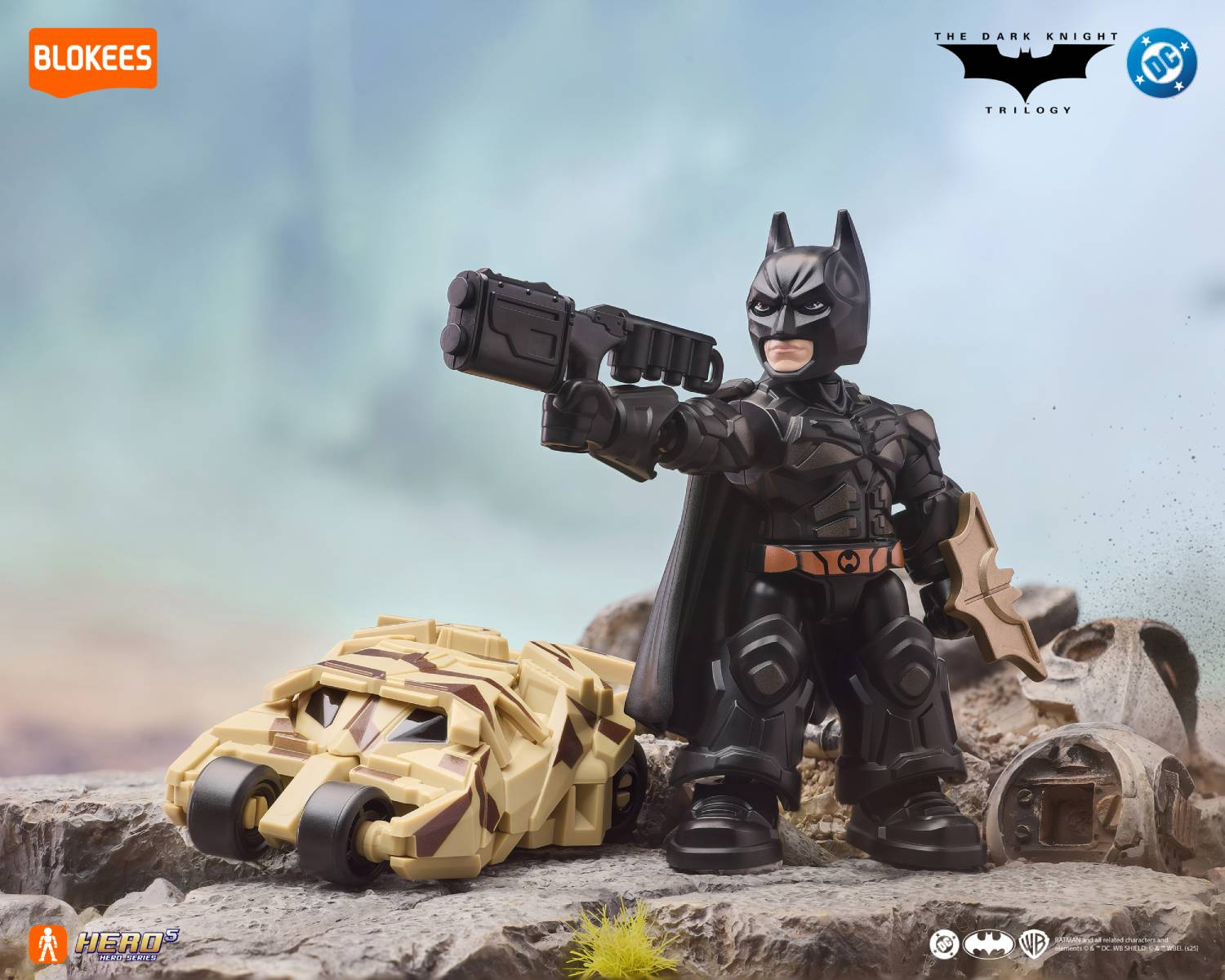 Figura de Batman con traje negro, arma y vehículo de camuflaje desértico en terreno rocoso.