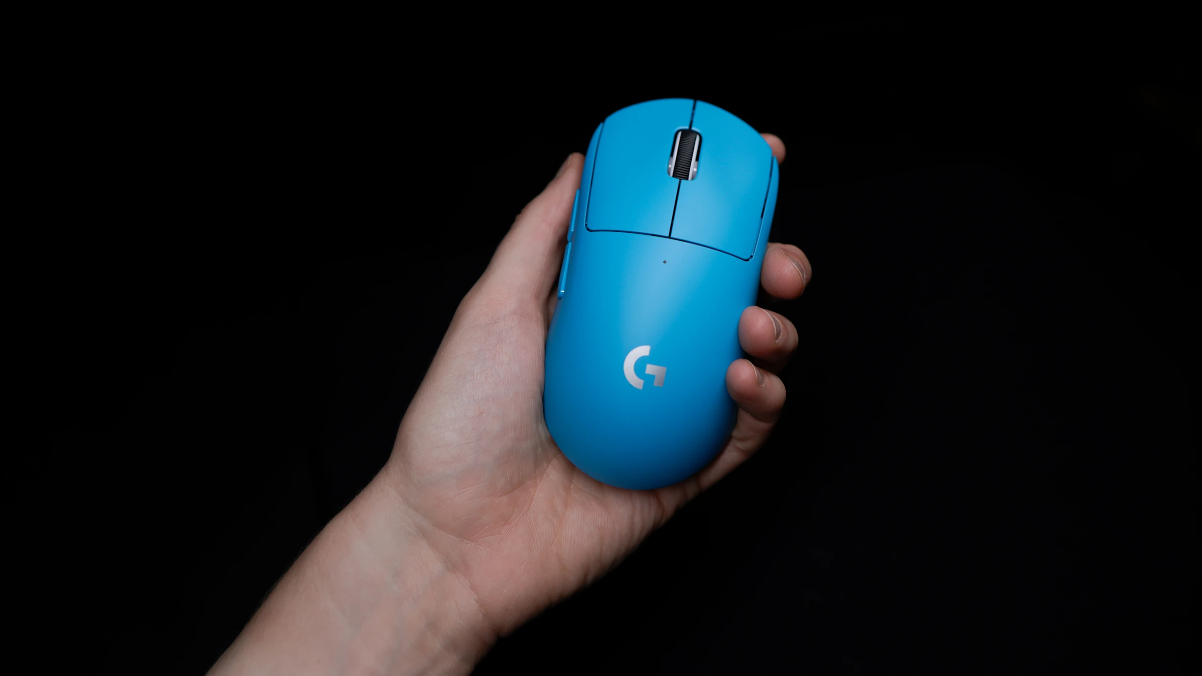 Egy kék Logitech egeret tartanak egy kézben fekete háttér előtt.