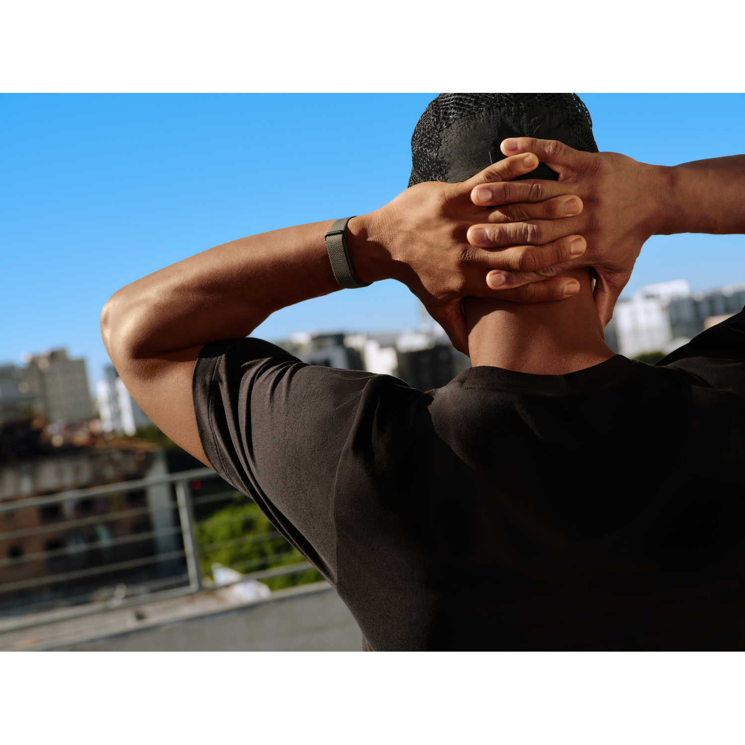 Man with hands behind head, looking at city in background, blue sky