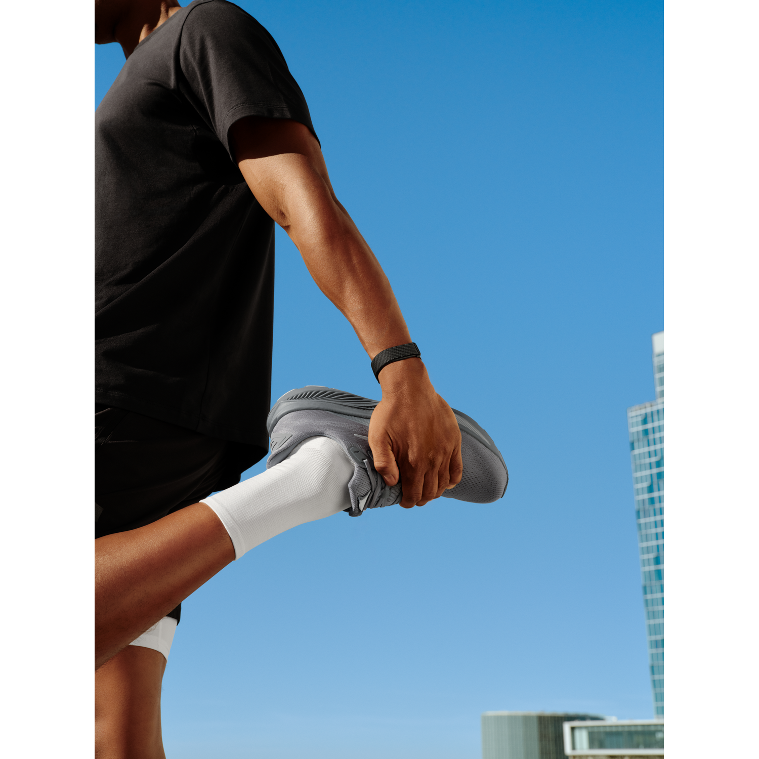 Man stretching outdoors with blue sky and buildings in the background.