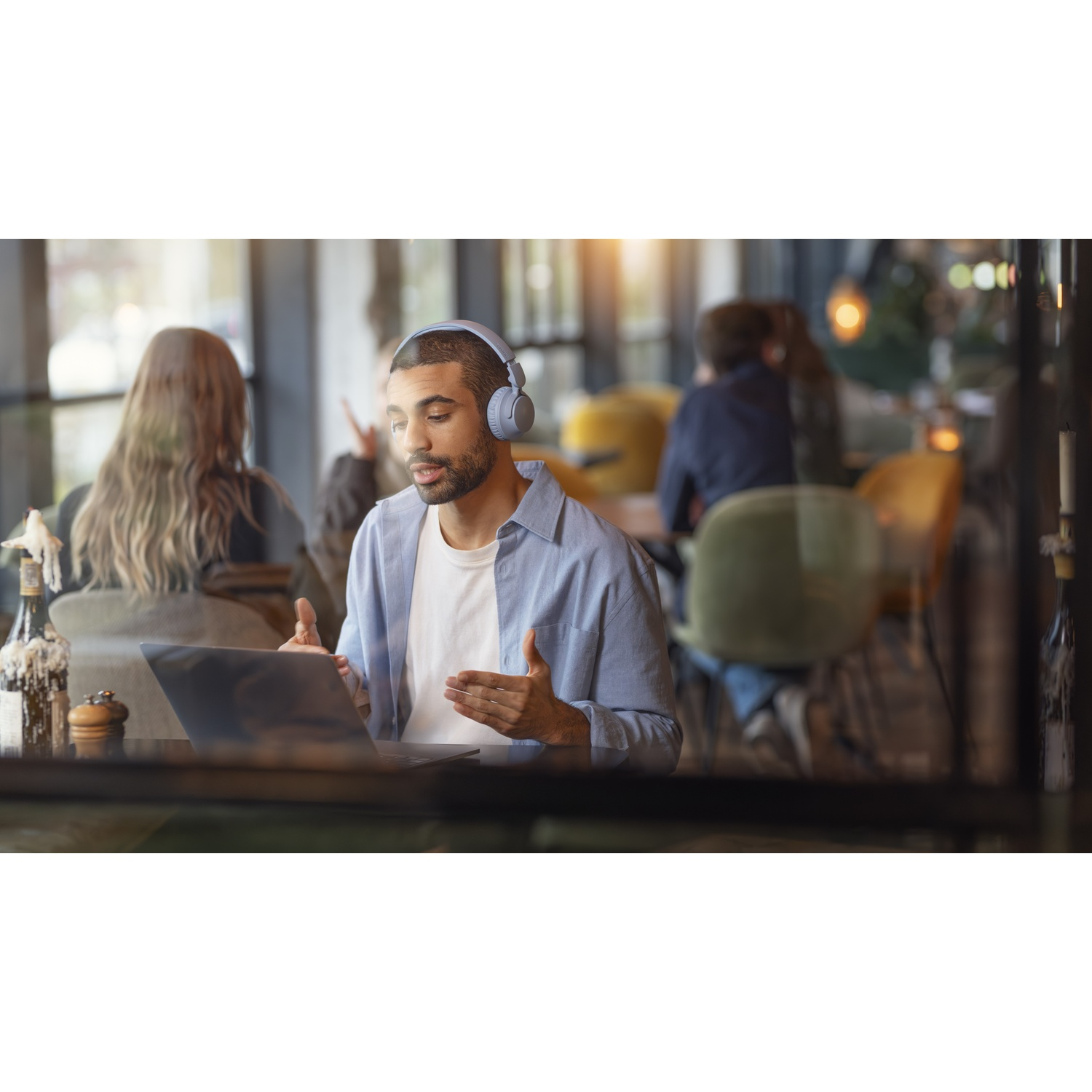 Uomo con cuffie parla online davanti a un laptop in un caffè.