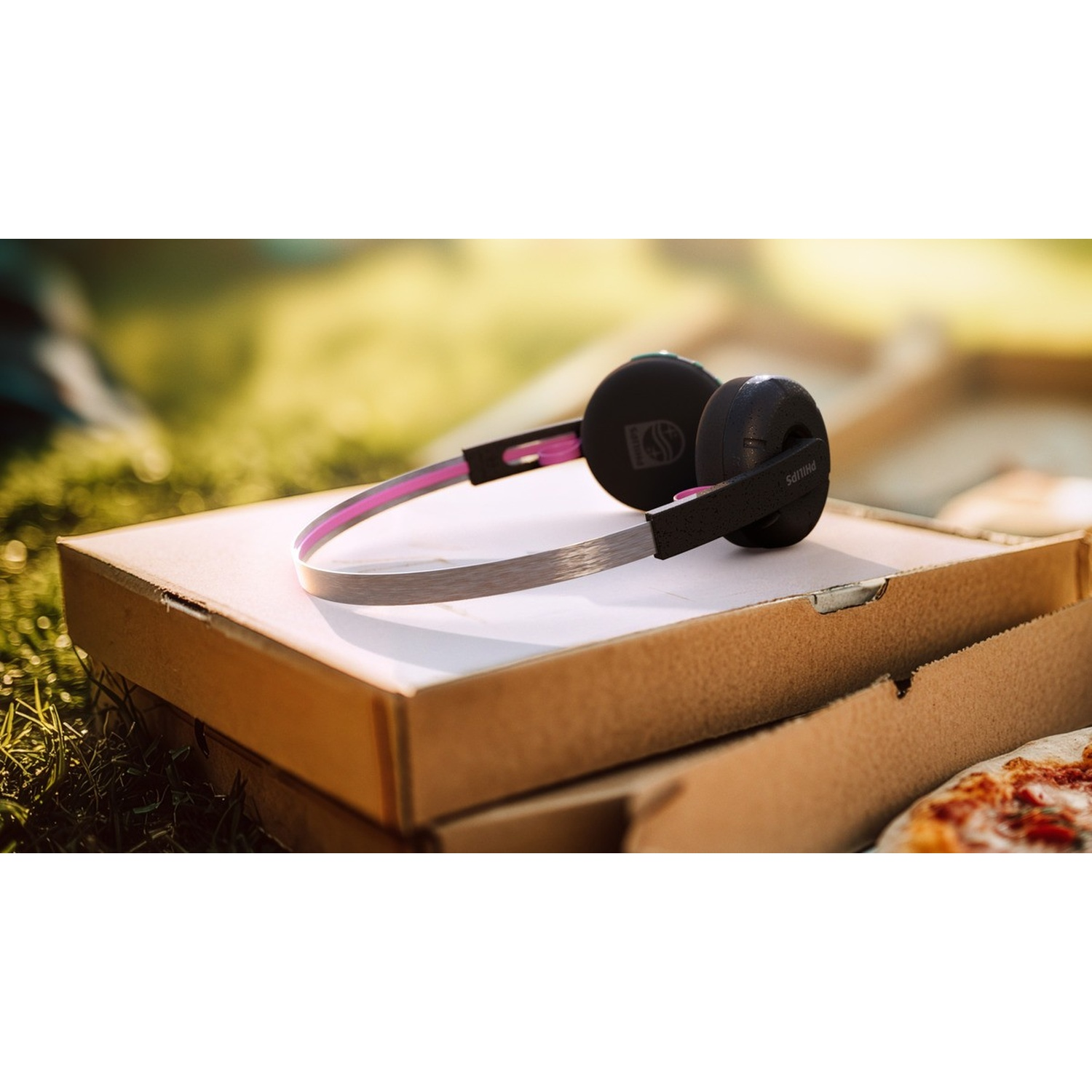 Cuffie nere con fascia rosa su cartoni della pizza sull'erba.