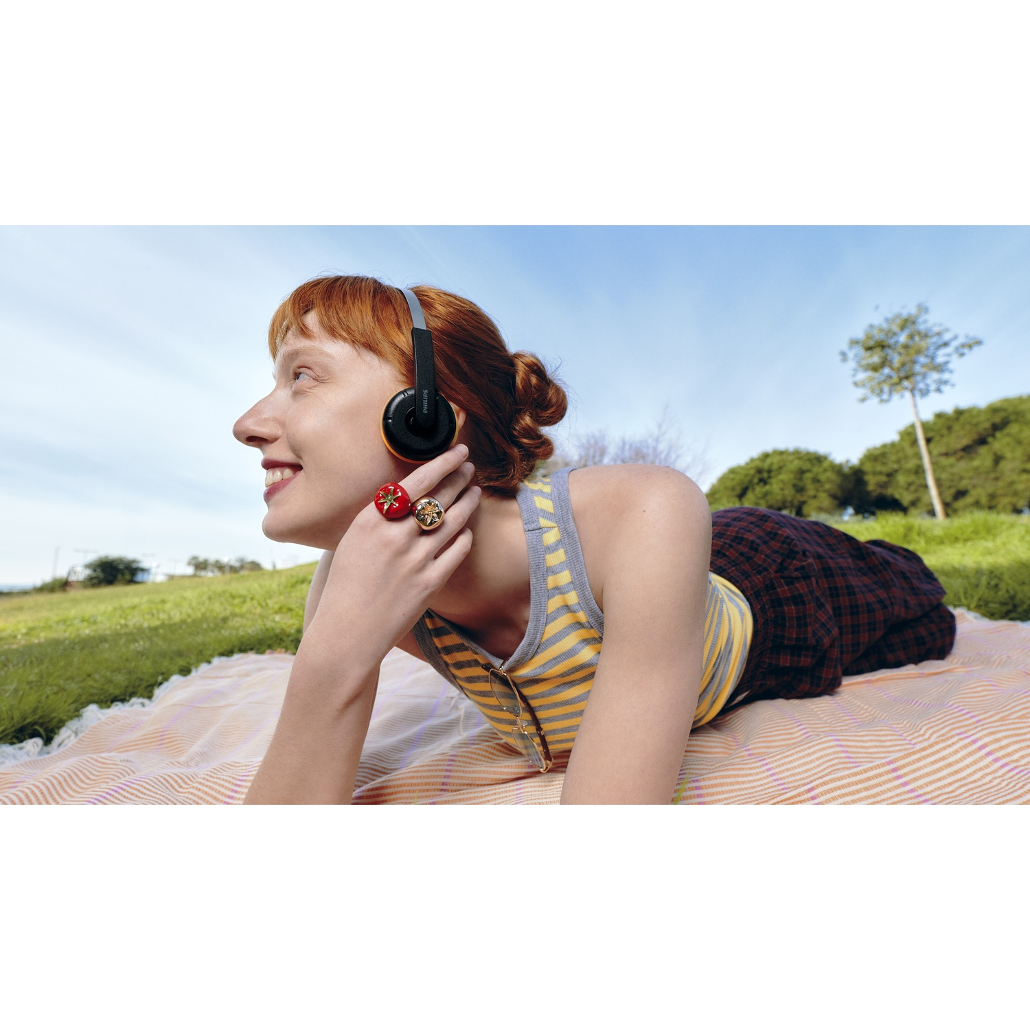 Donna con capelli rossi giace su una coperta all'aperto, indossa cuffie e ascolta musica.