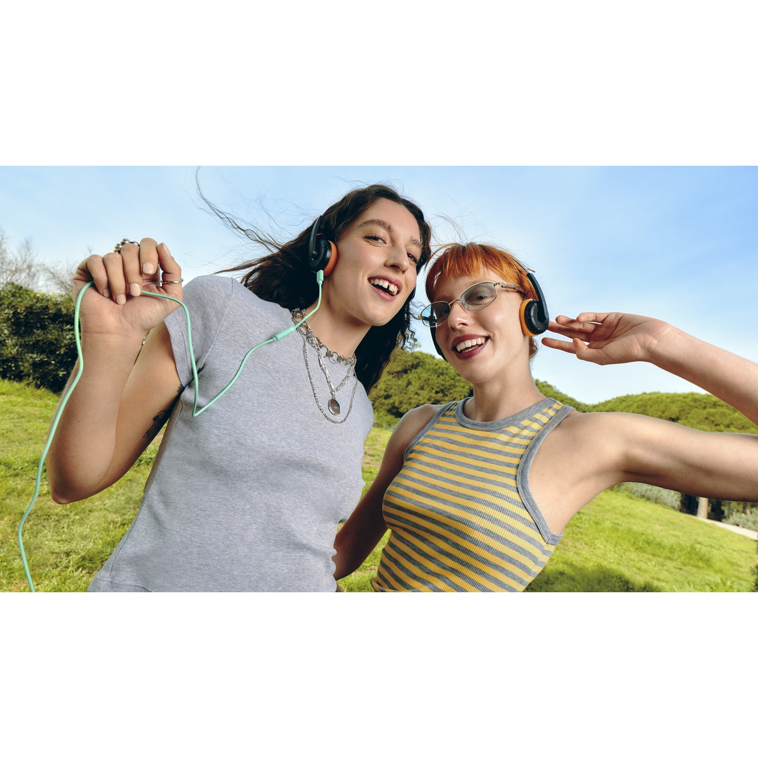 Due giovani donne con cuffie in piedi all'aperto, sorridenti.