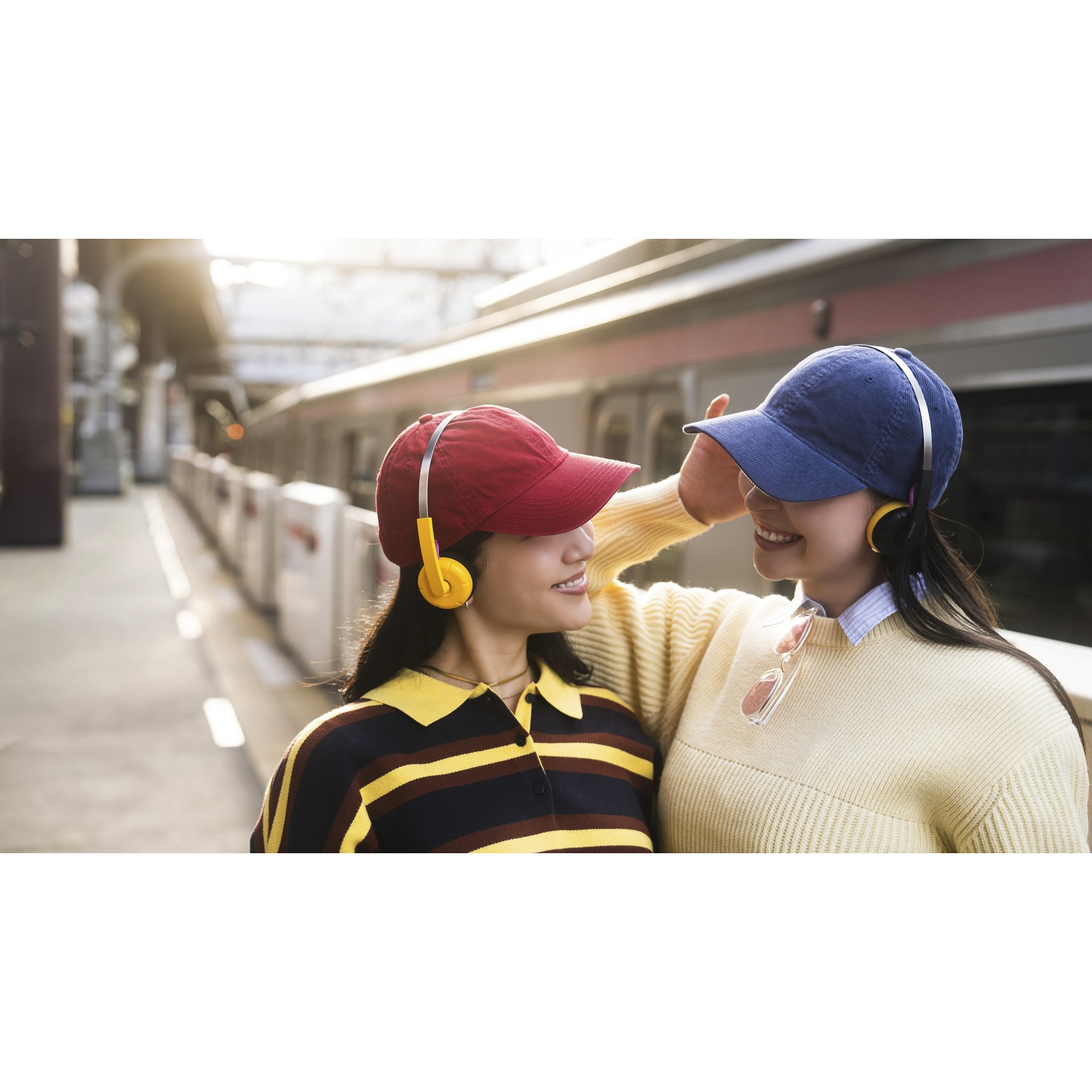 Due giovani donne con cuffie e cappelli su una banchina.