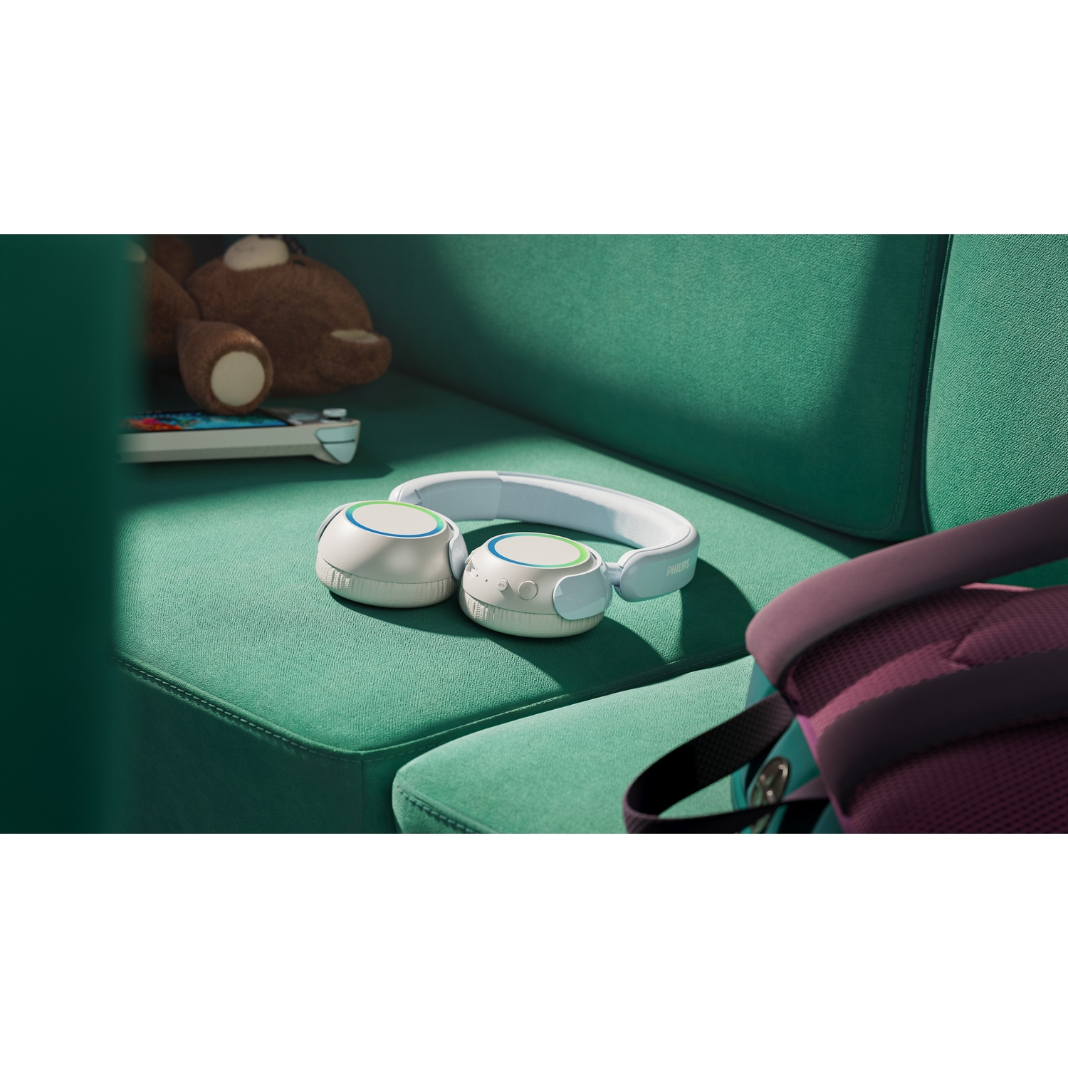 Cuffie bianche su un divano verde accanto a un orsacchiotto e un controller.