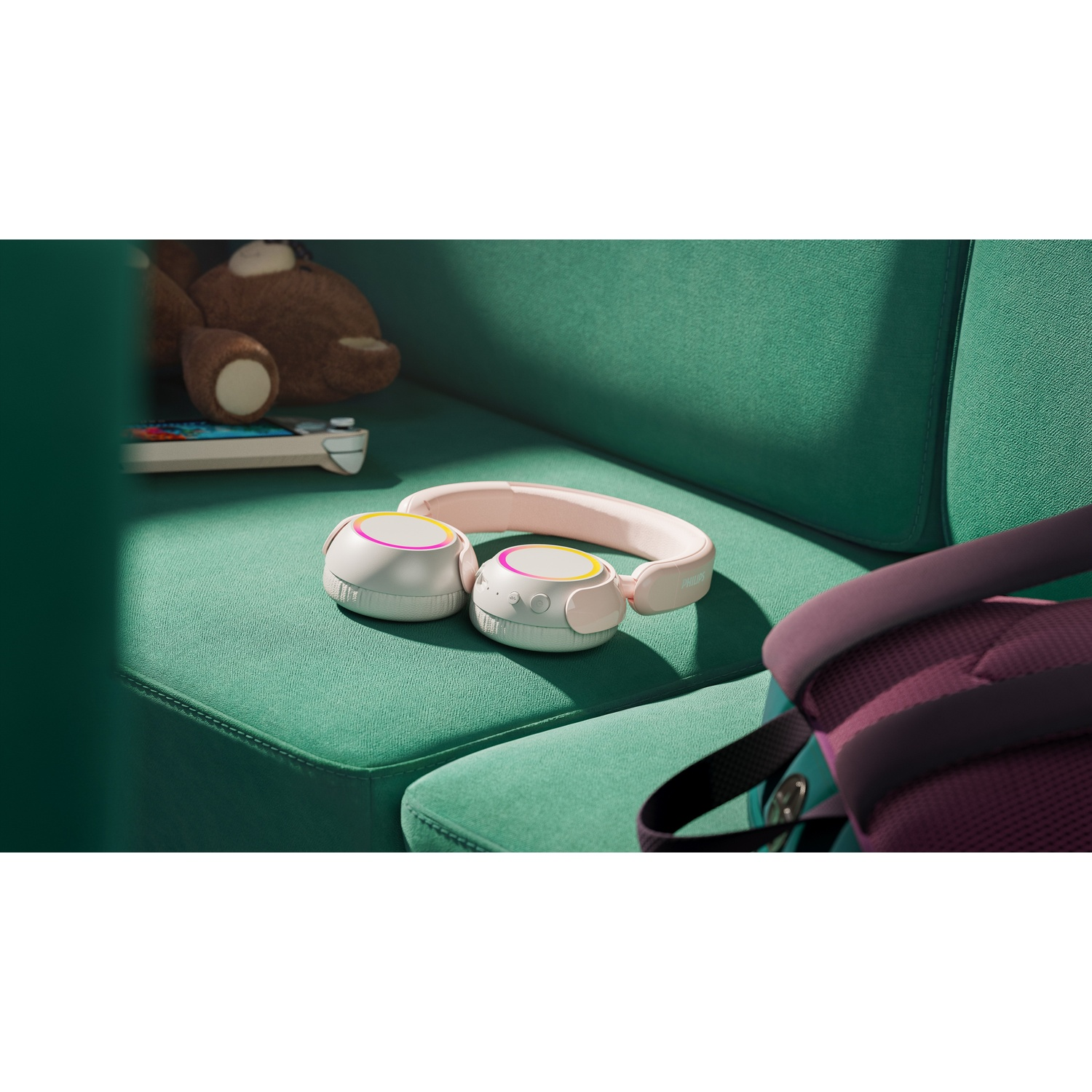 Orsacchiotto, console di gioco e cuffie su un divano verde.